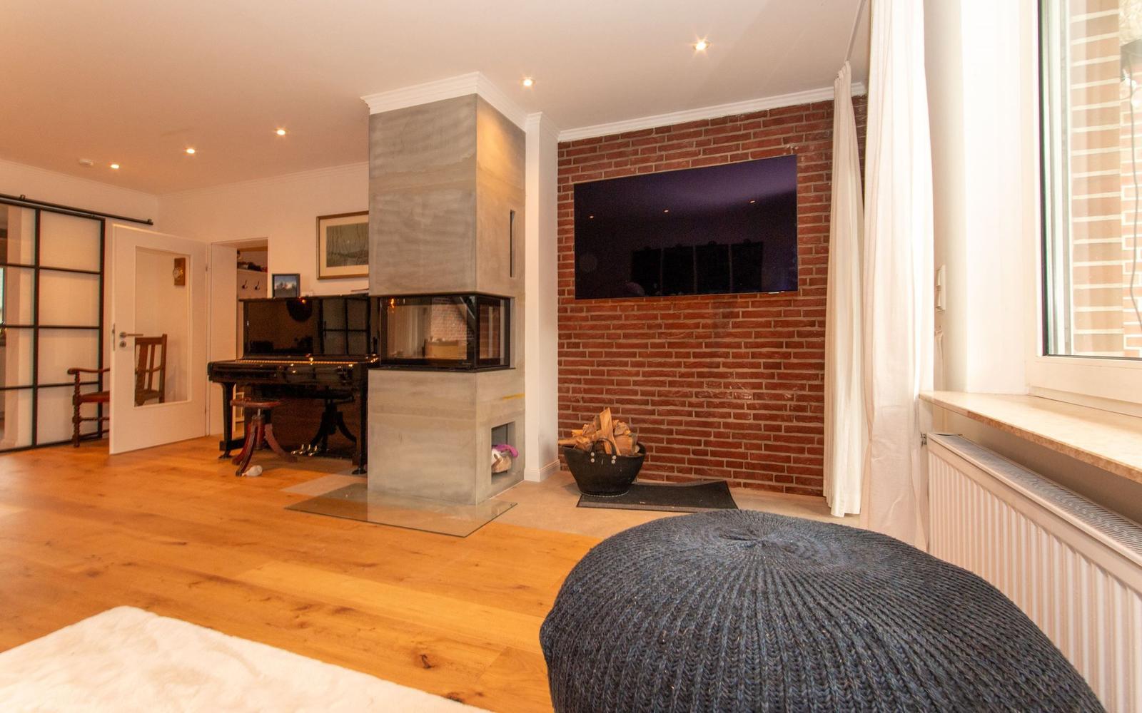 Wohnraum mit Kamin, Klavier und Fernseher an Backsteinwand.