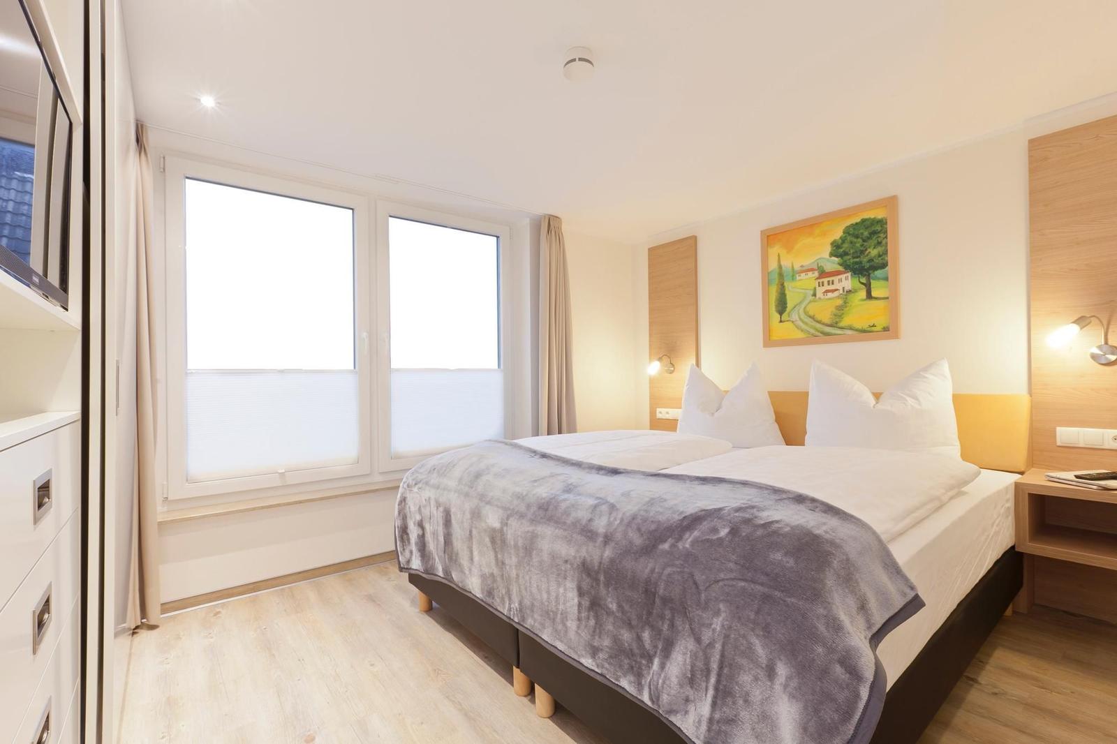 Schlafzimmer mit Doppelbett, Fenster und Wandbild.