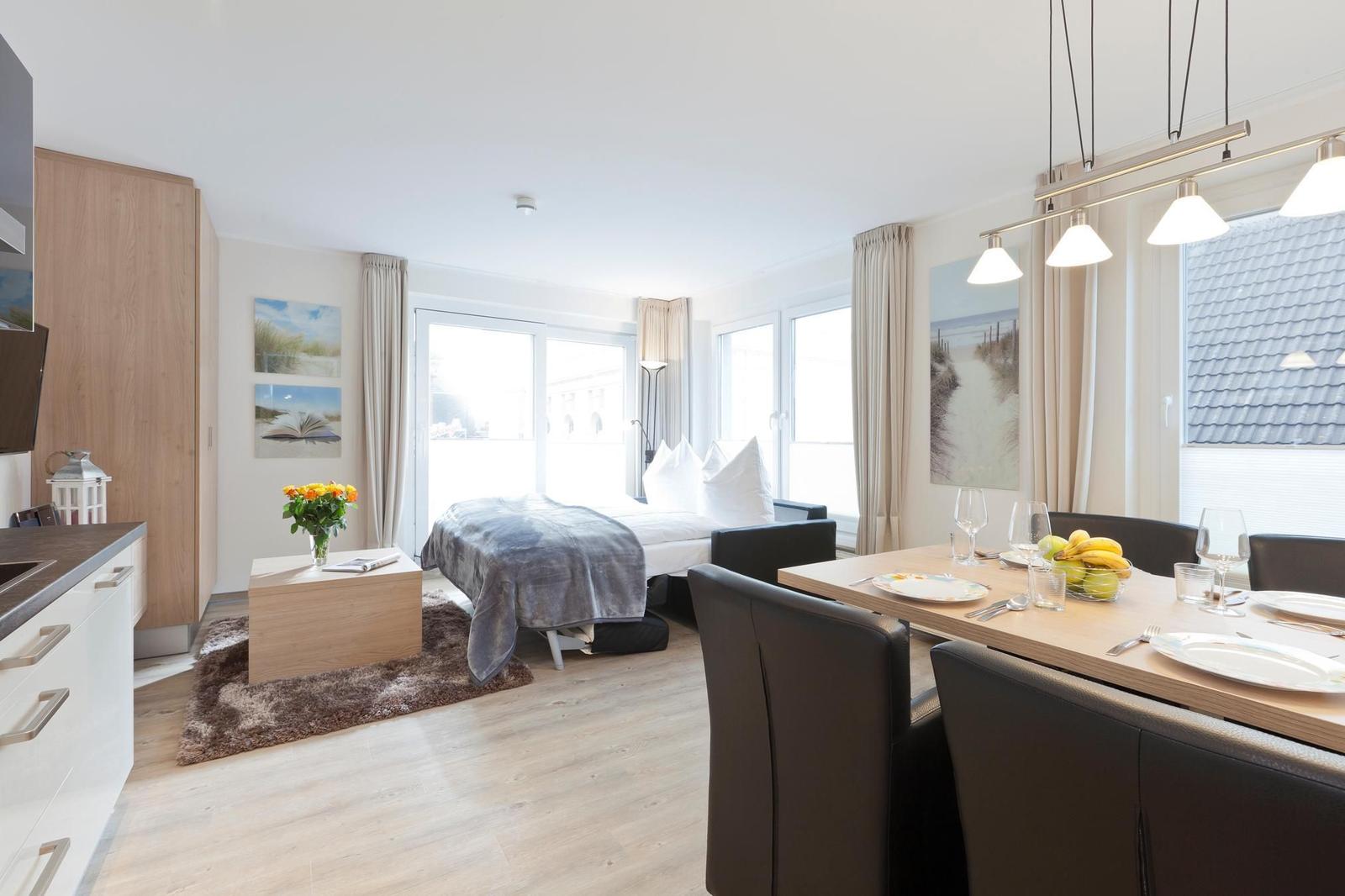 Wohnung mit Schlafzimmer, Essbereich und Küchenzeile. Fenster mit Blick auf Außenbereich.