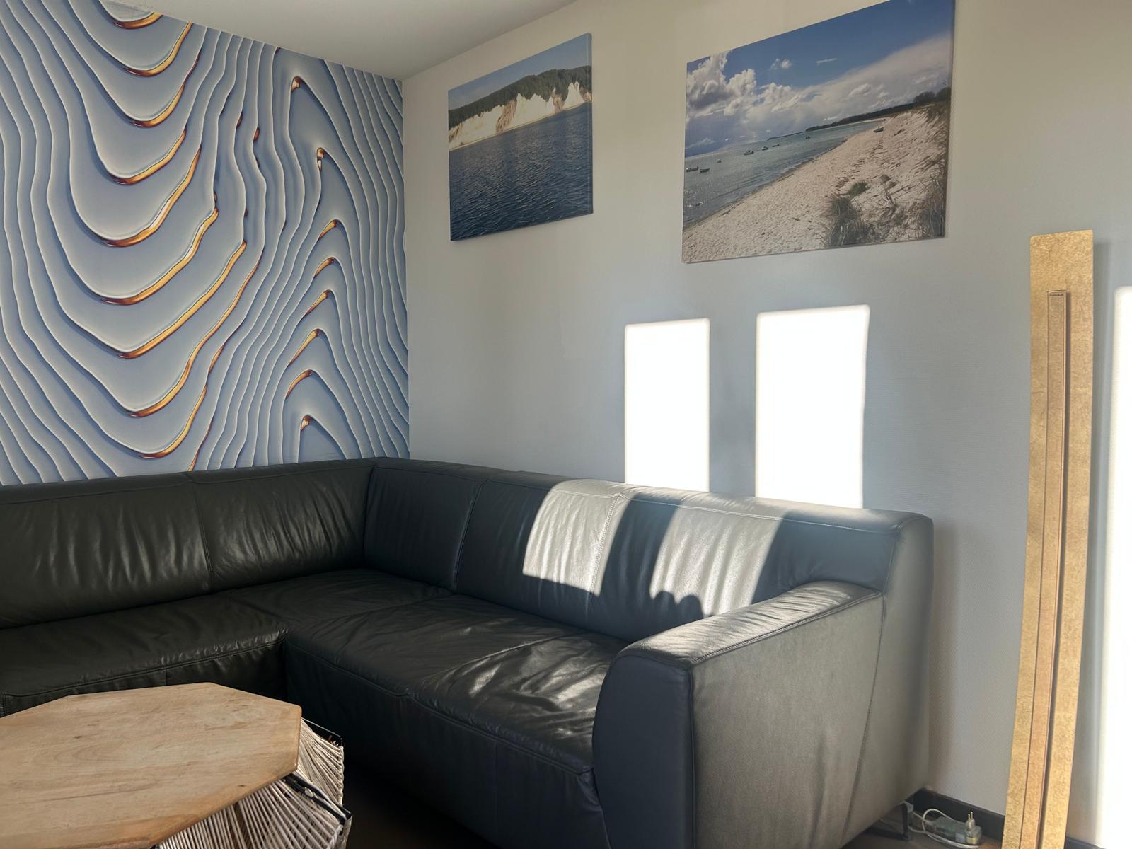 Schwarzes Ledersofa vor Wand mit 3D-Relief und Strandbildern an der Wand.