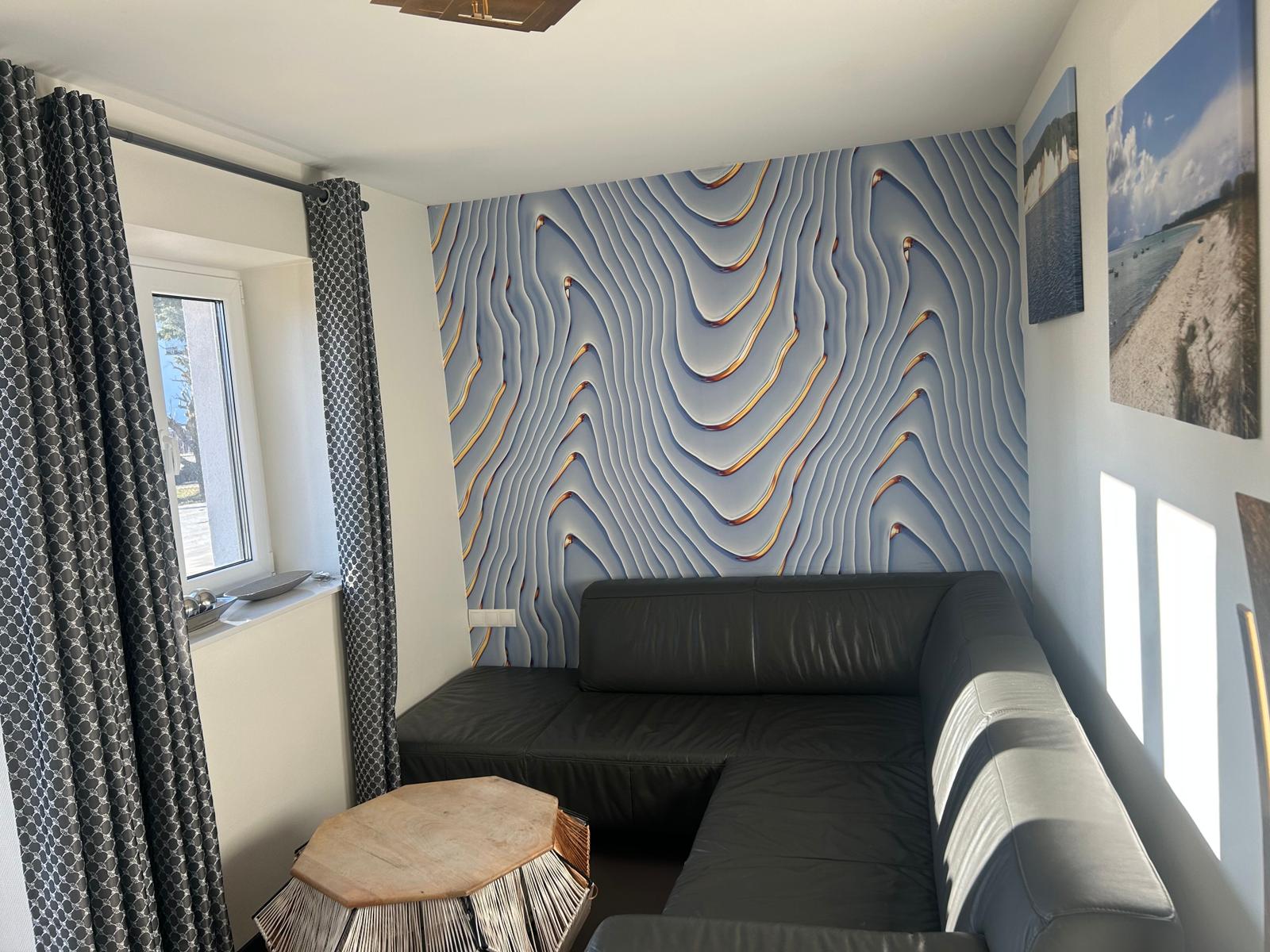 Schwarzes Sofa vor einer wellenförmigen Wand. Fenster mit Vorhängen. Tisch aus Holz.