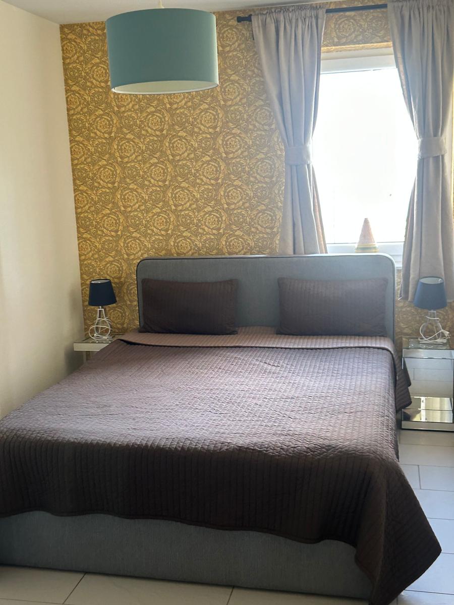 Schlafzimmer mit Bett, Nachttischen und Fenster mit Vorhängen.