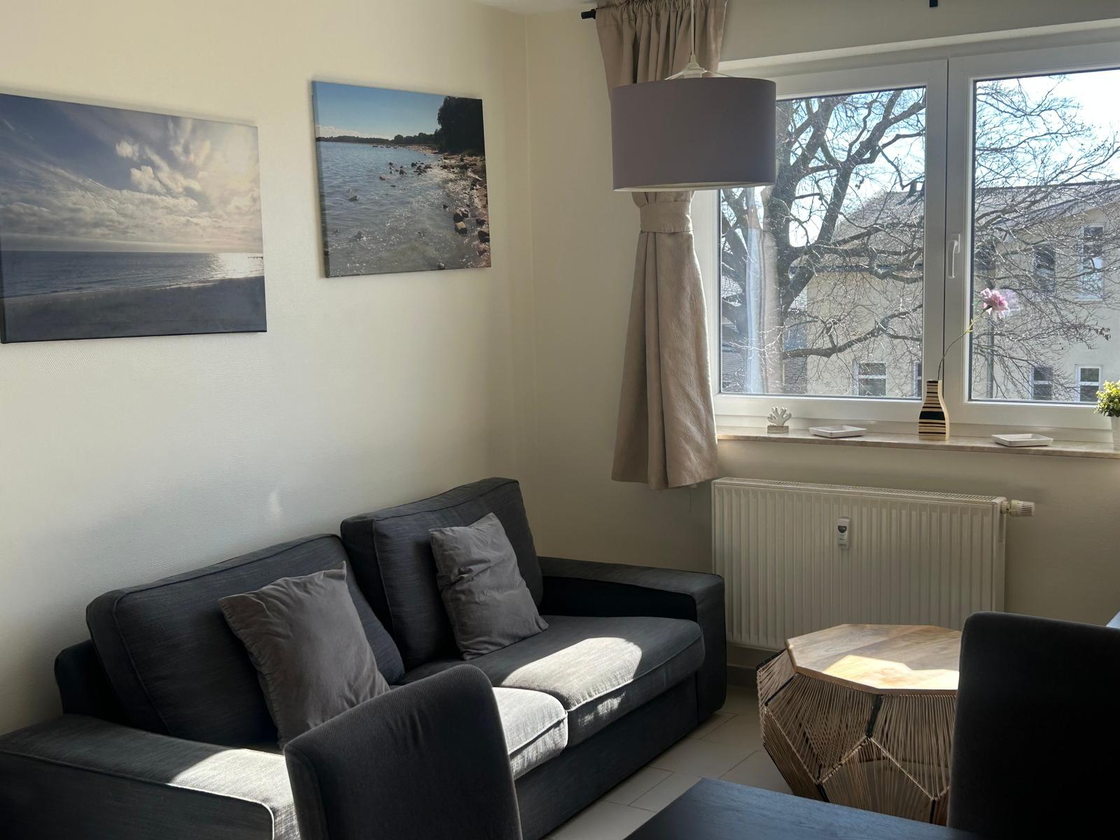 Ein Wohnzimmer mit Sofa, Fenster und Wandbildern.