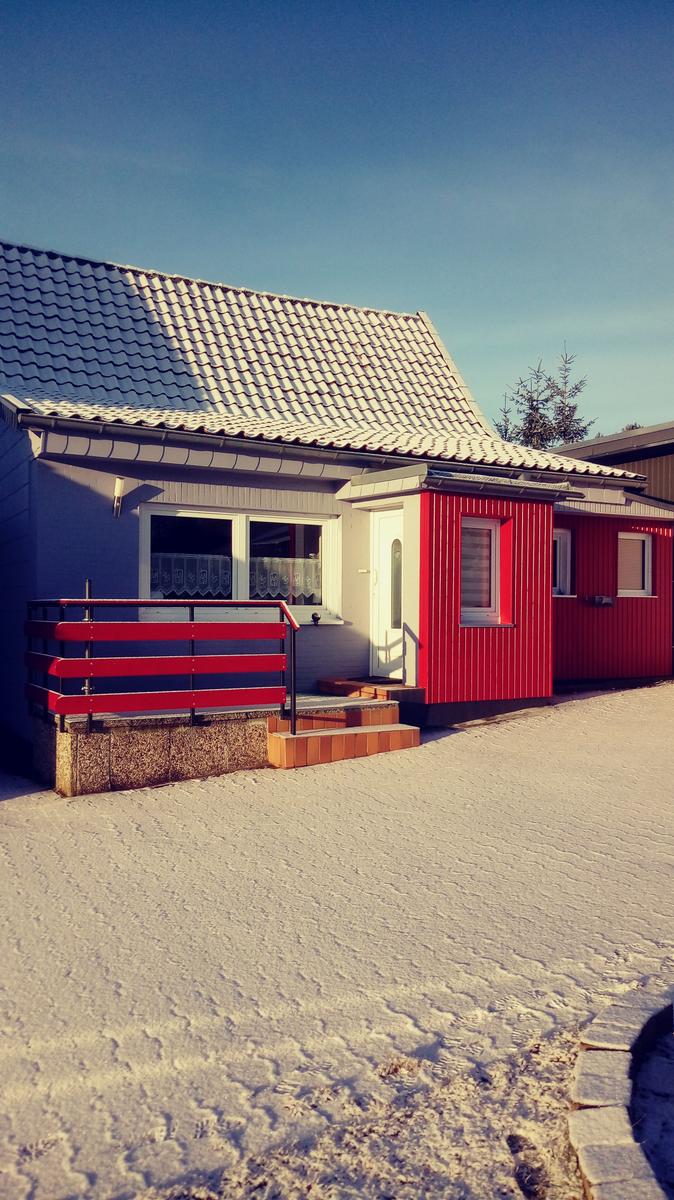 Ein Haus mit rotem Anbau und weißem Dach steht auf schneebedecktem Boden.