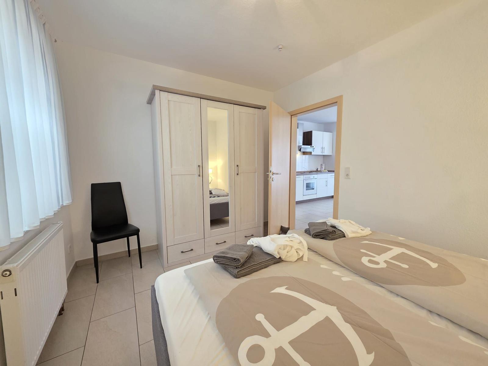 Schlafzimmer mit Bett, Kleiderschrank und Blick in die Küche.