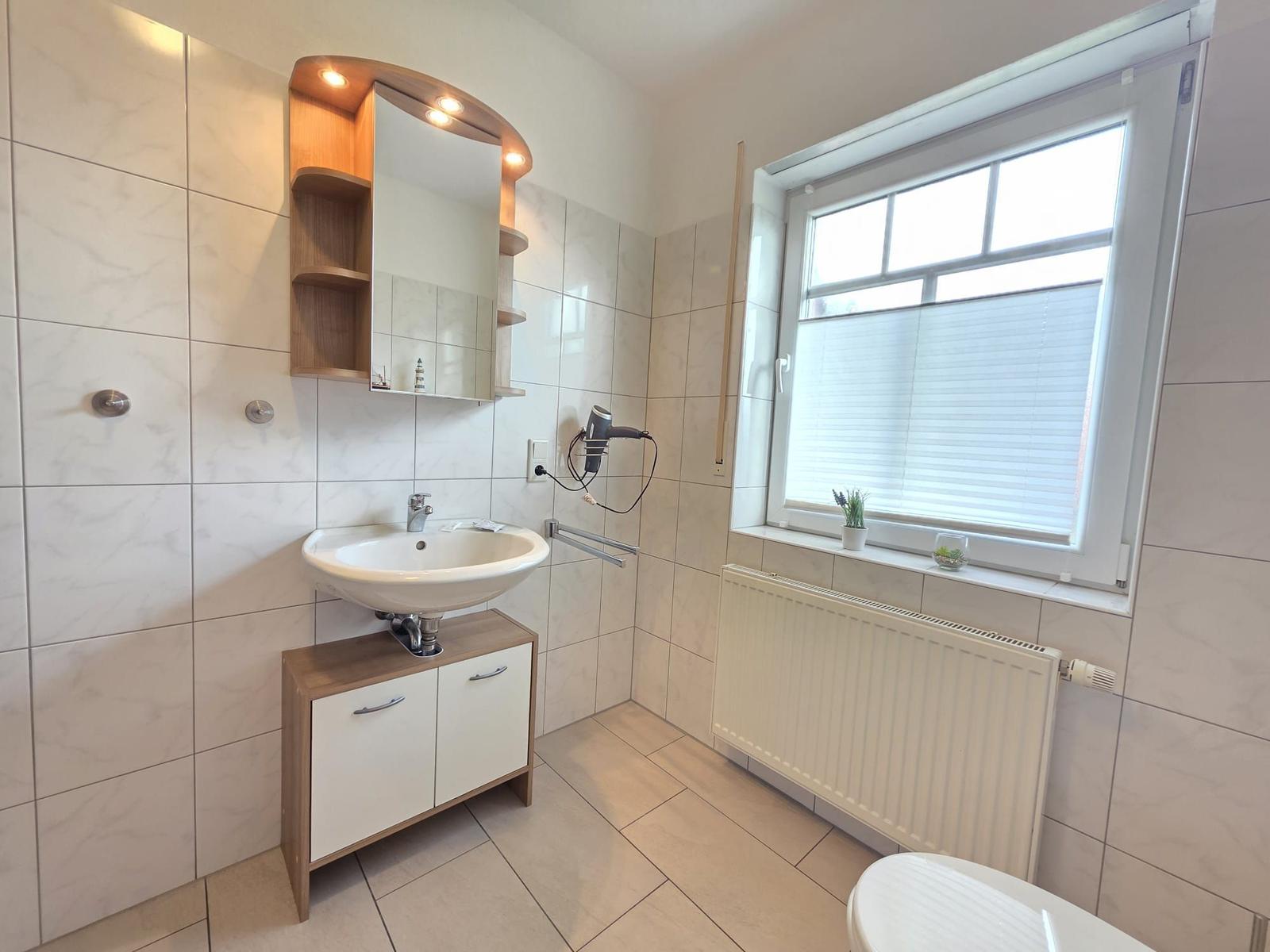 Badezimmer mit Waschbecken, Spiegel, Fenster und Heizkörper.