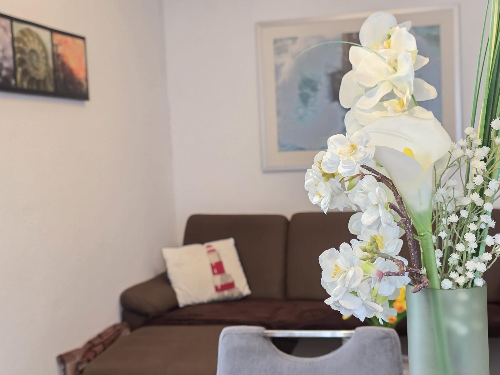 Ein Wohnzimmer mit braunem Sofa, Kissen und Blumenvase.
