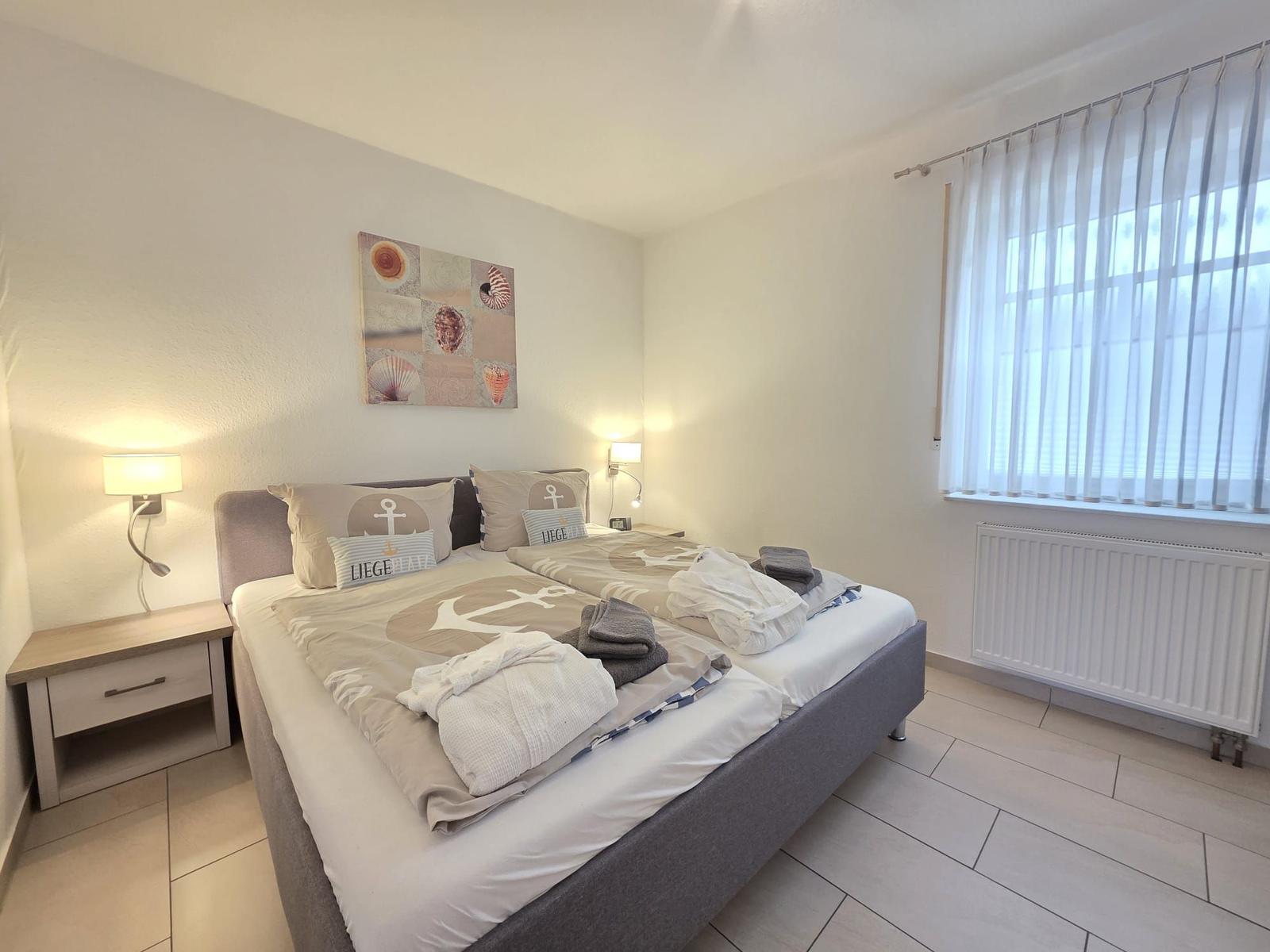 Schlafzimmer mit Doppelbett, Nachttischen und Fenster mit Vorhängen.