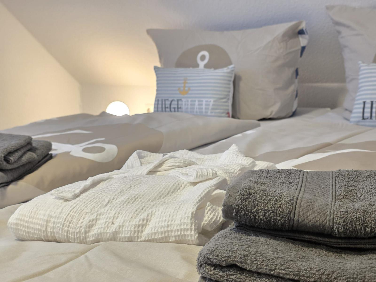 Doppelbett mit Bettwäsche, Kissen und gefalteten Handtüchern.