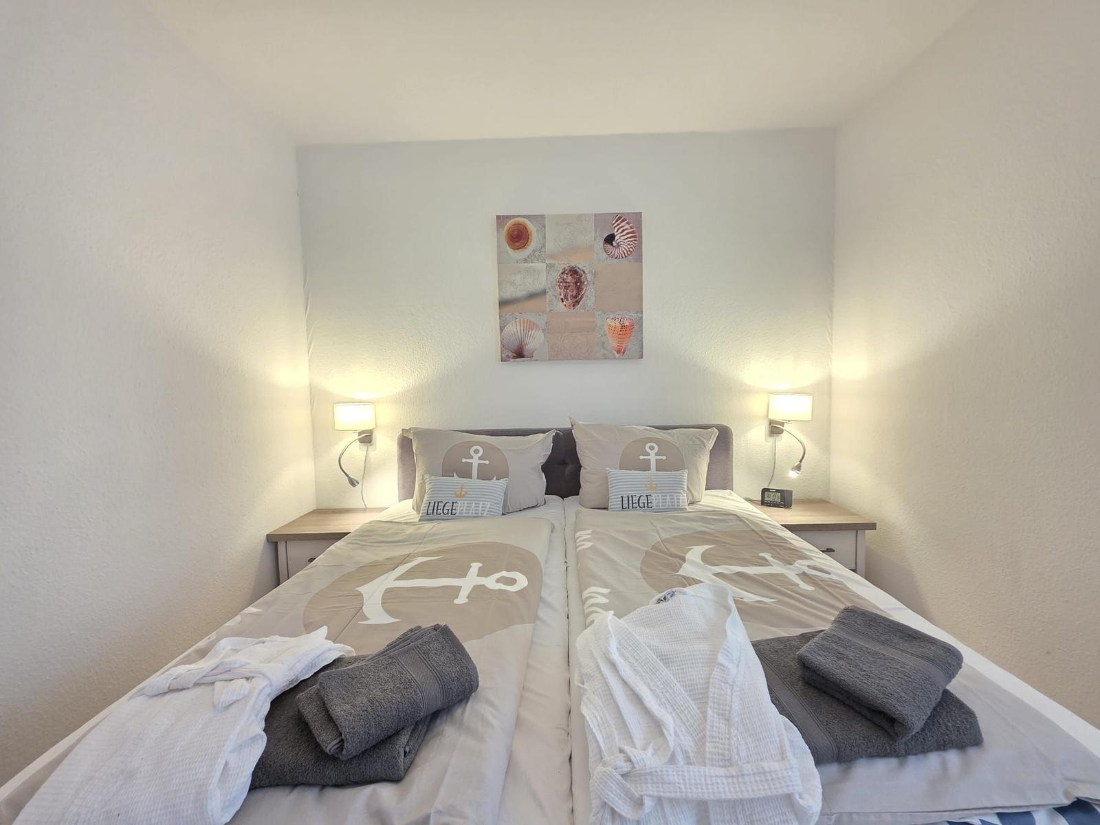 Zimmer mit zwei Betten, Seemotiv-Bettwäsche und Wandbild mit Muscheln.
