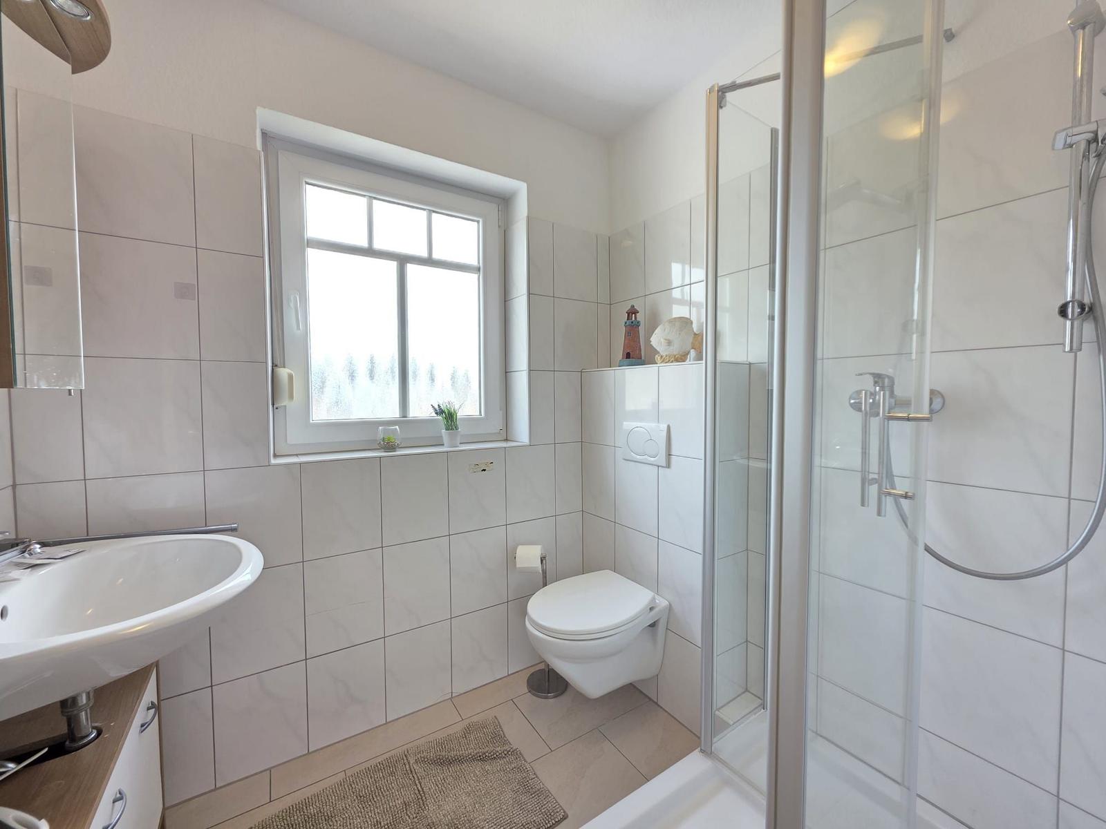 Bathroom with shower, toilet, and sink. Window with view outside.
