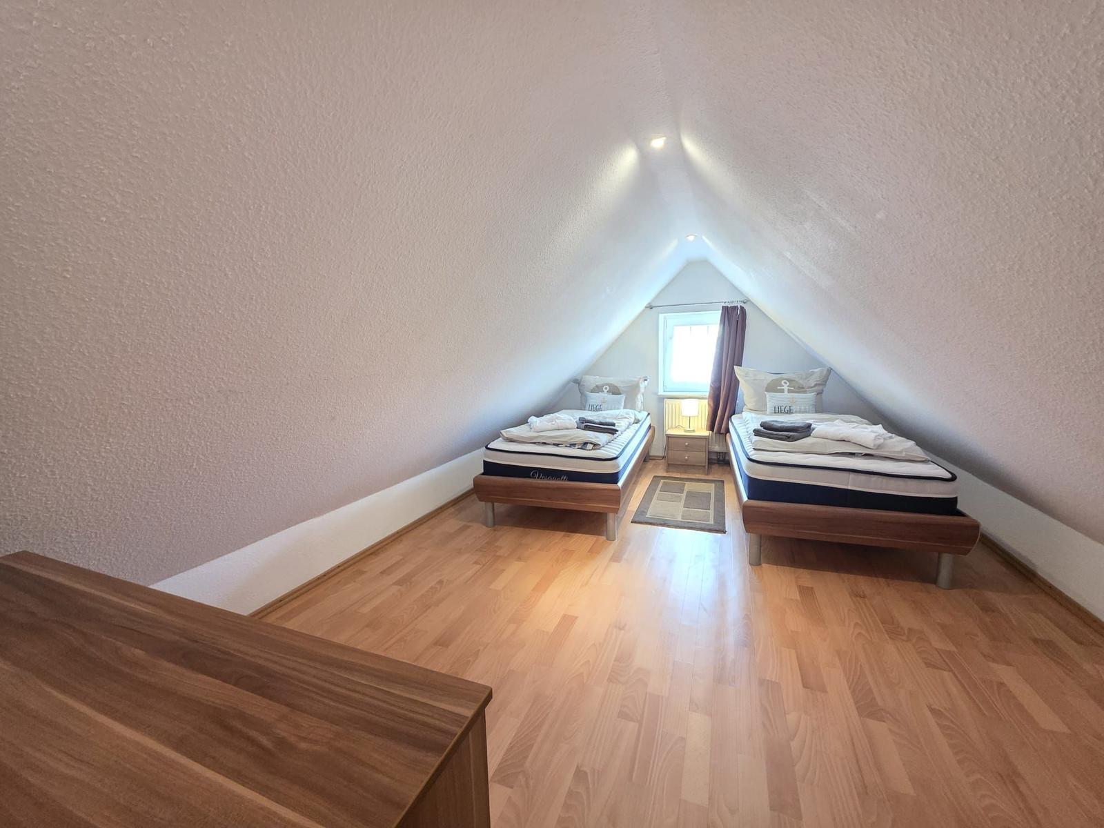 Two beds in an attic room with wooden floor and window.