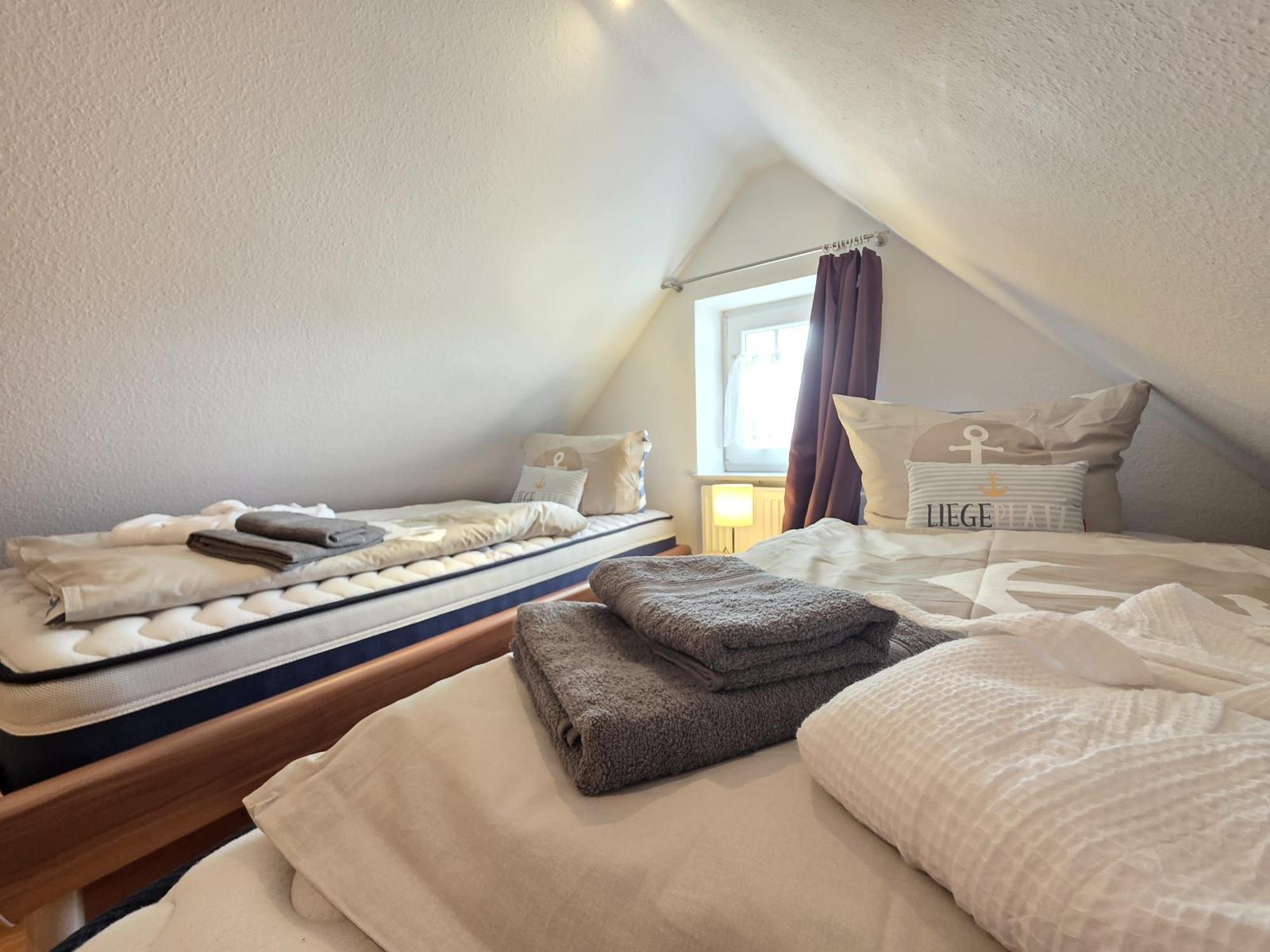 Two beds with bedding and towels under sloped ceilings.