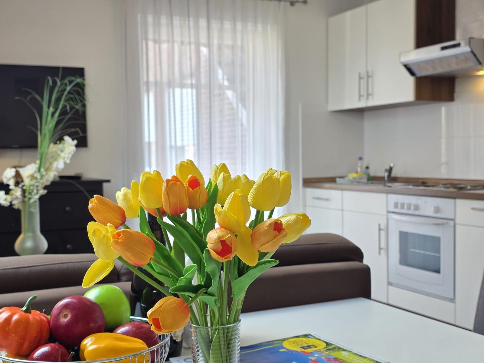 Kitchen and living area with flowers, fruit, and TV.