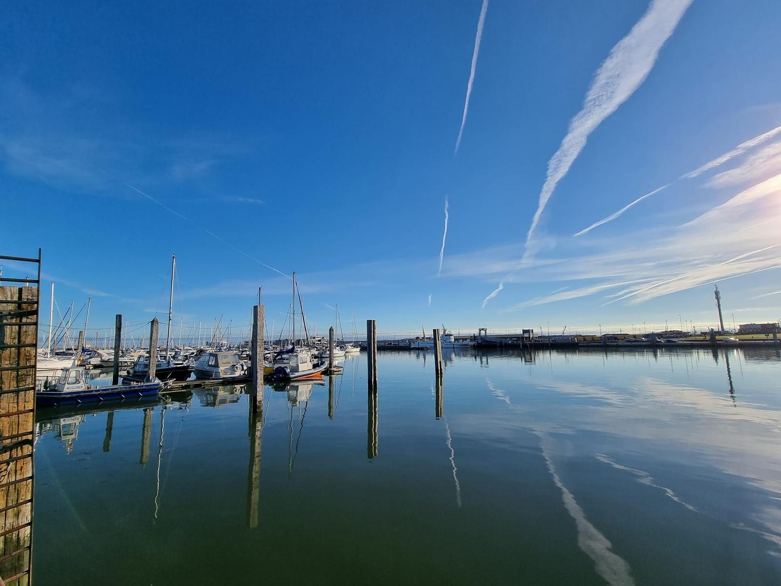 Harbor with boats and clear sky with contrails.
