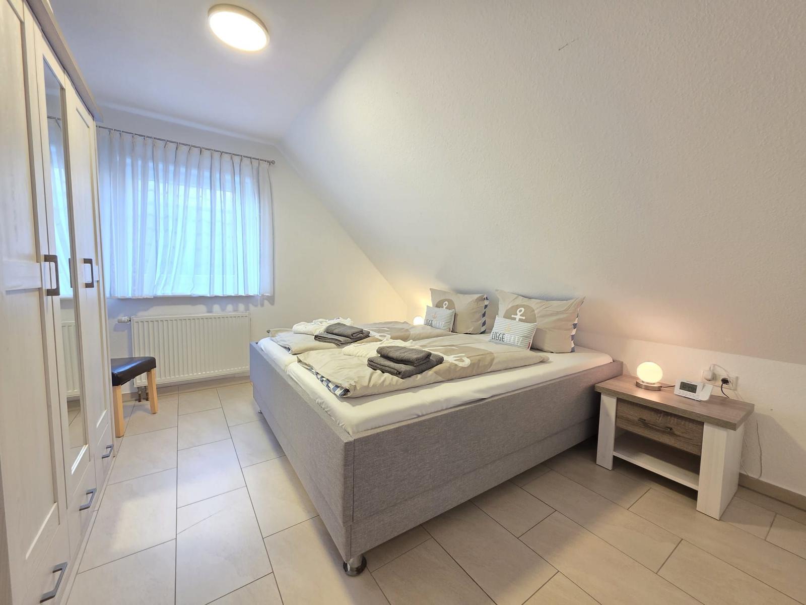 Bedroom with double bed, nightstand, and wardrobe. Window with curtains.