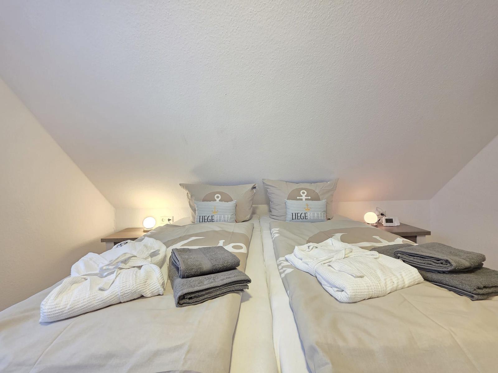 Two beds with bathrobes and towels under sloped ceiling