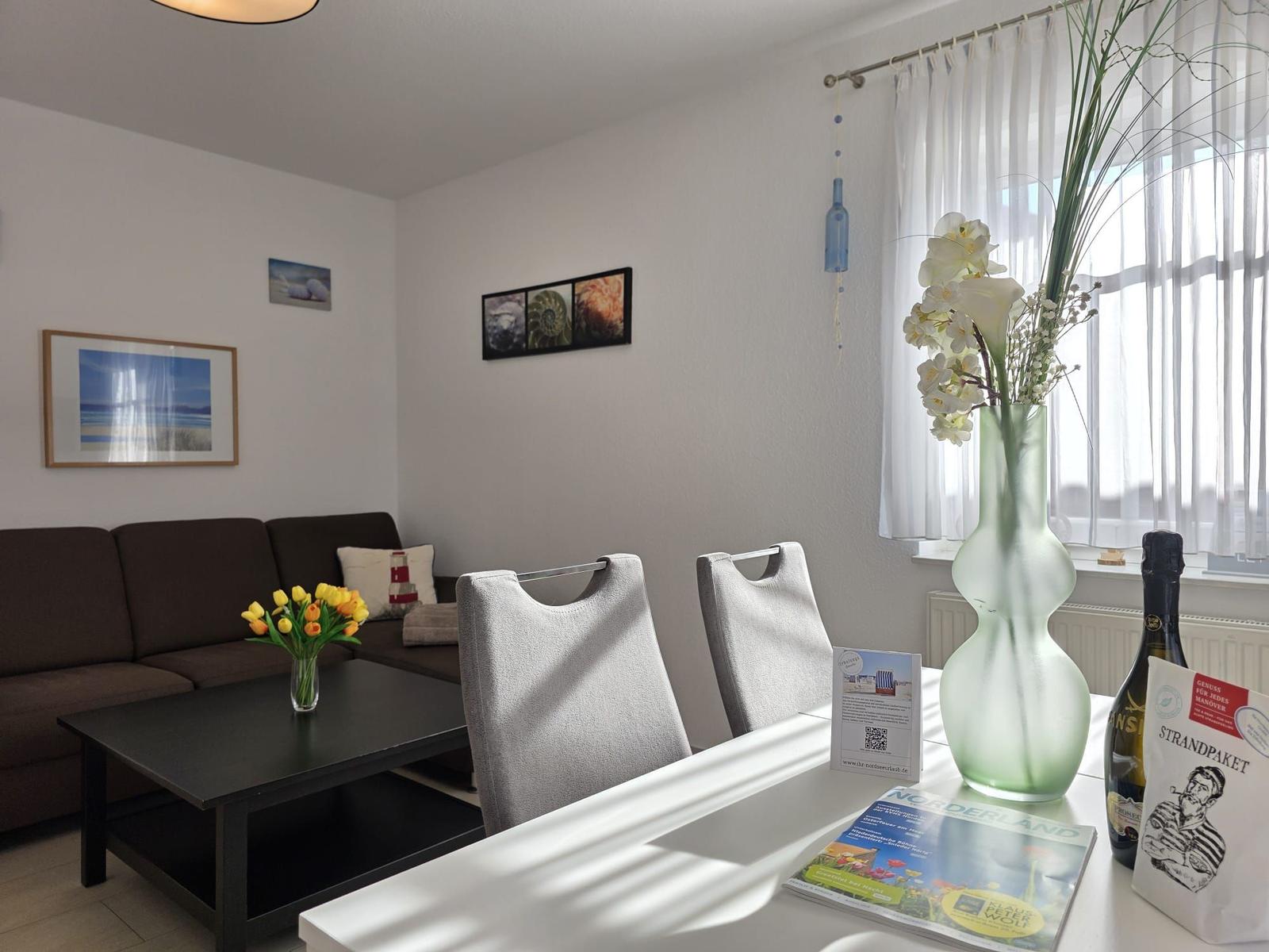 Living and dining area with sofa, table, and chairs. Window with white curtains.