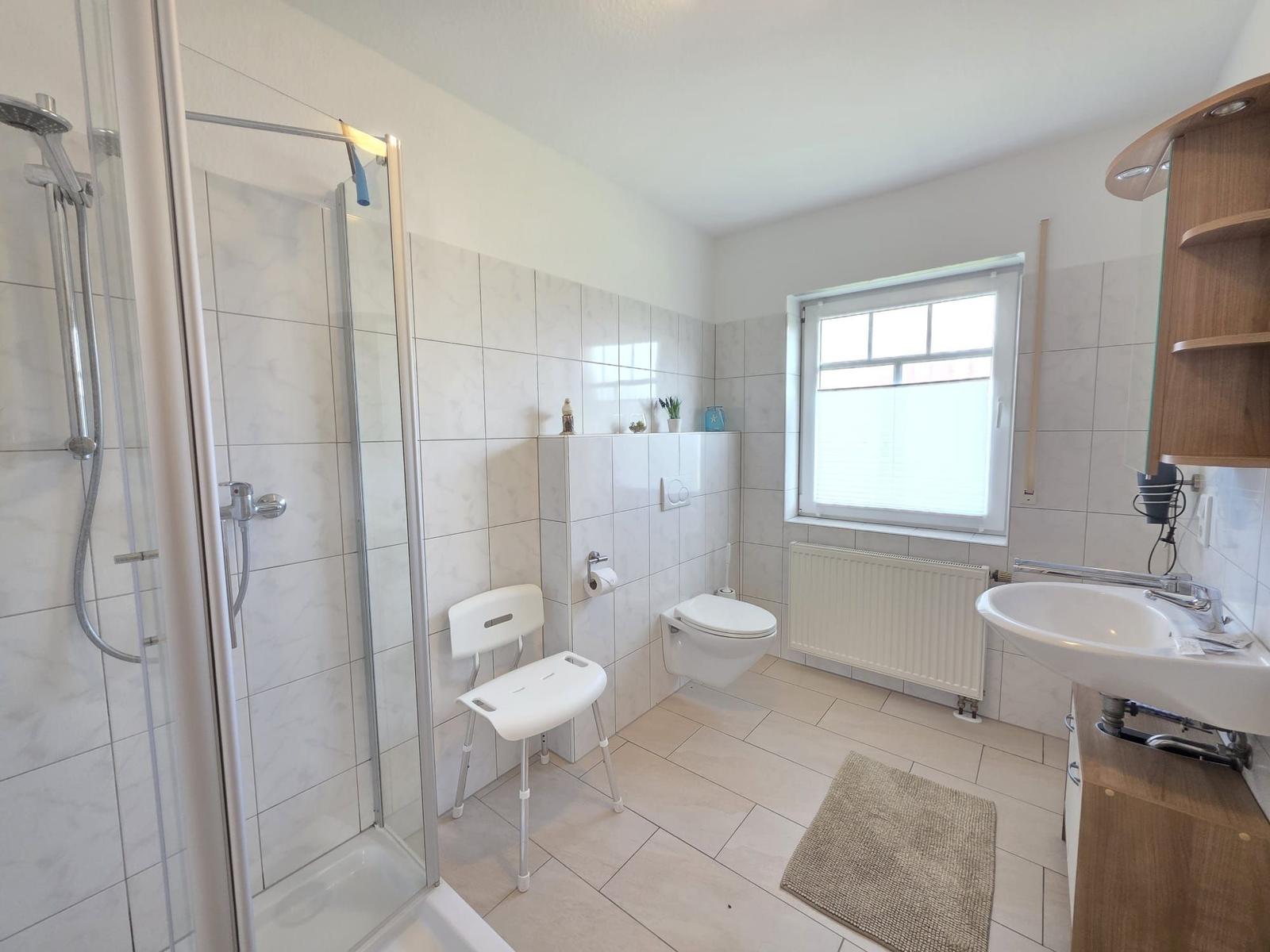 Bathroom with shower, toilet, and sink. Window and radiator visible.