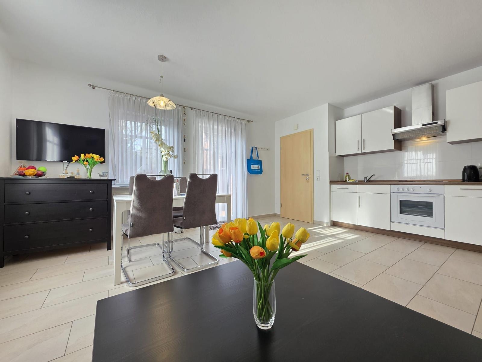Kitchen with dining area and TV. Vase with tulips on table.