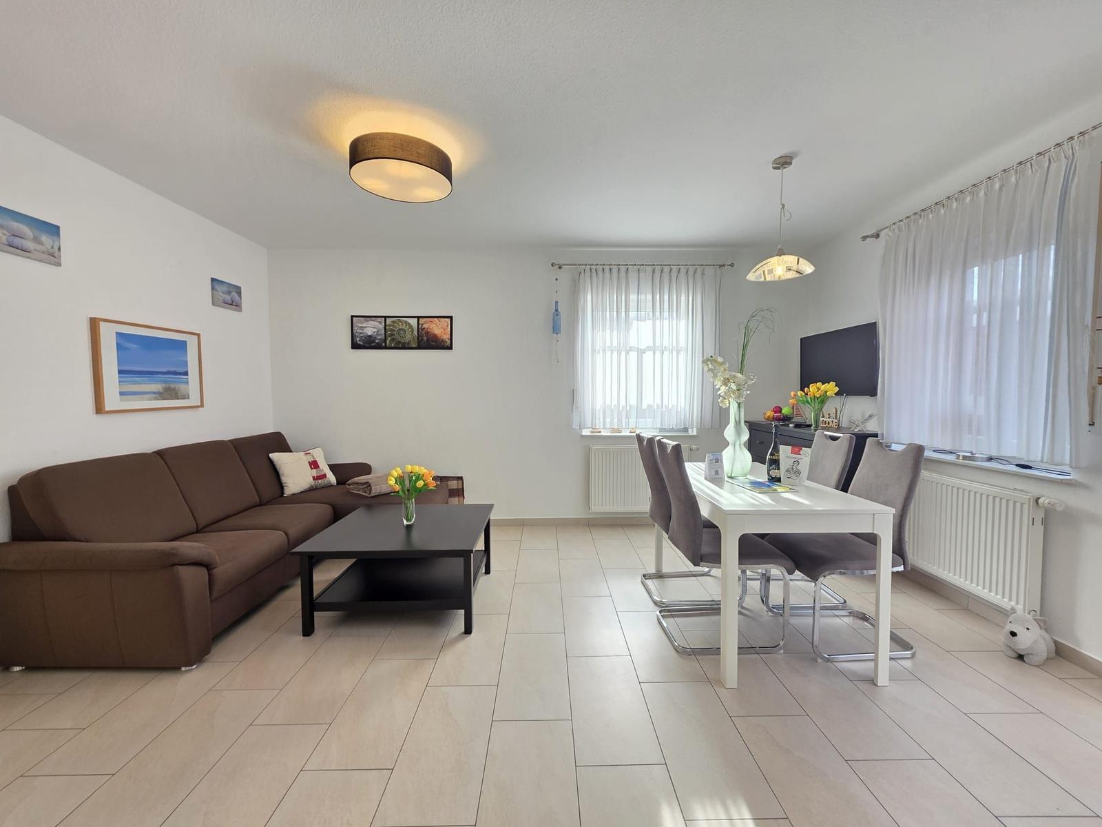 Living and dining area with sofa, table and chairs. Windows with curtains.