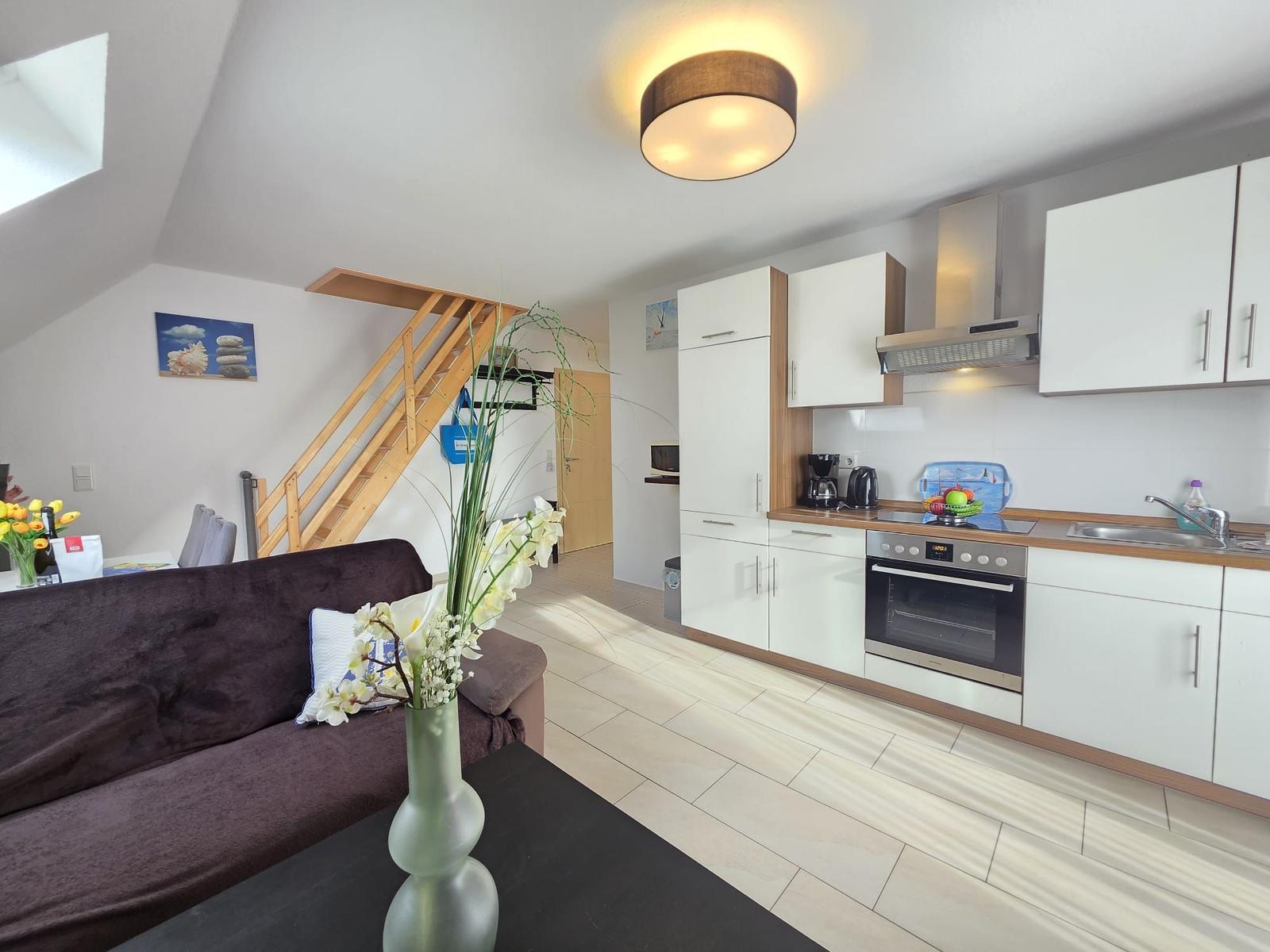 Living area with kitchen, sofa, and stairs to upper floor.