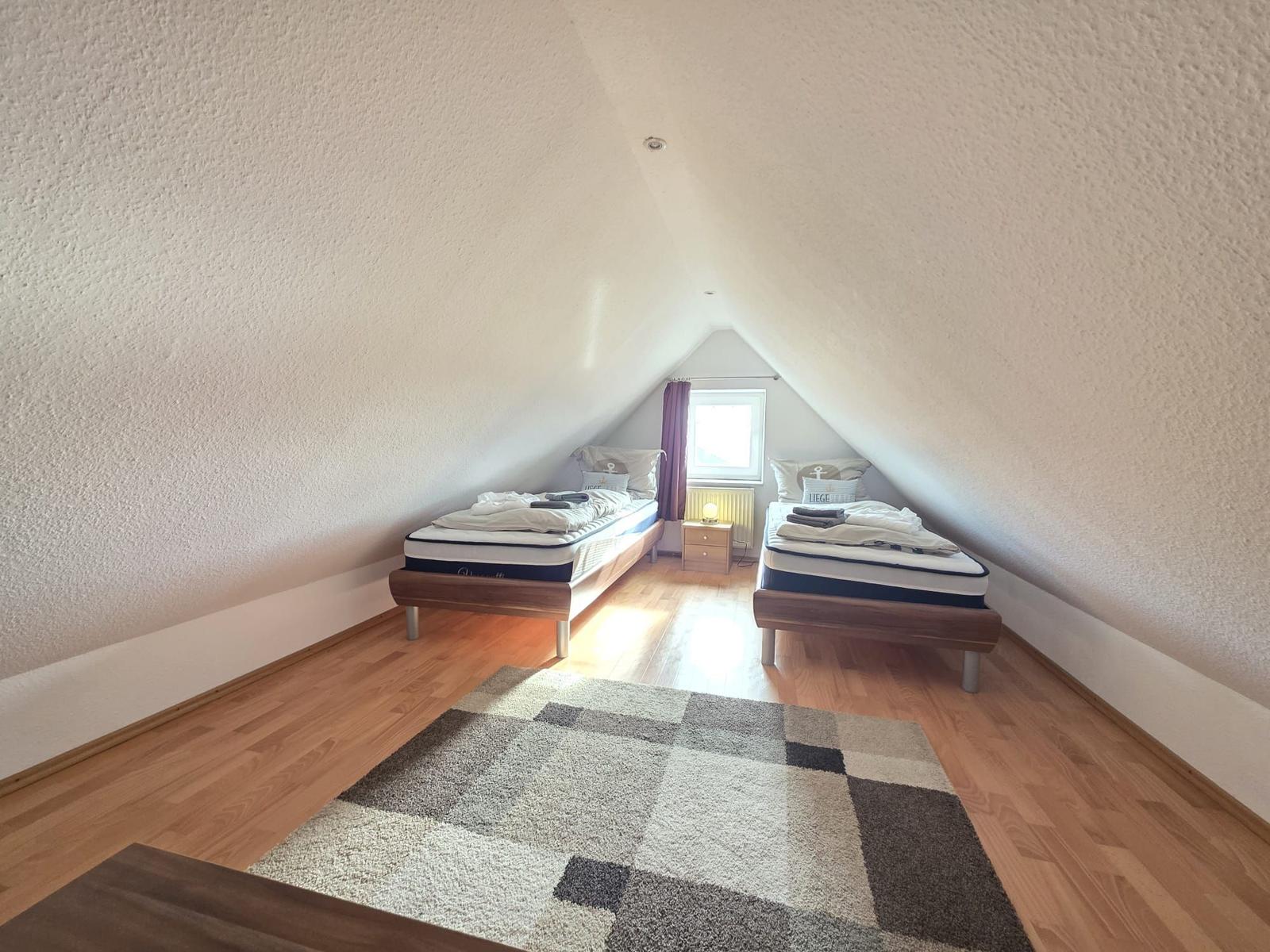 Two beds in an attic room with wooden floor and window.