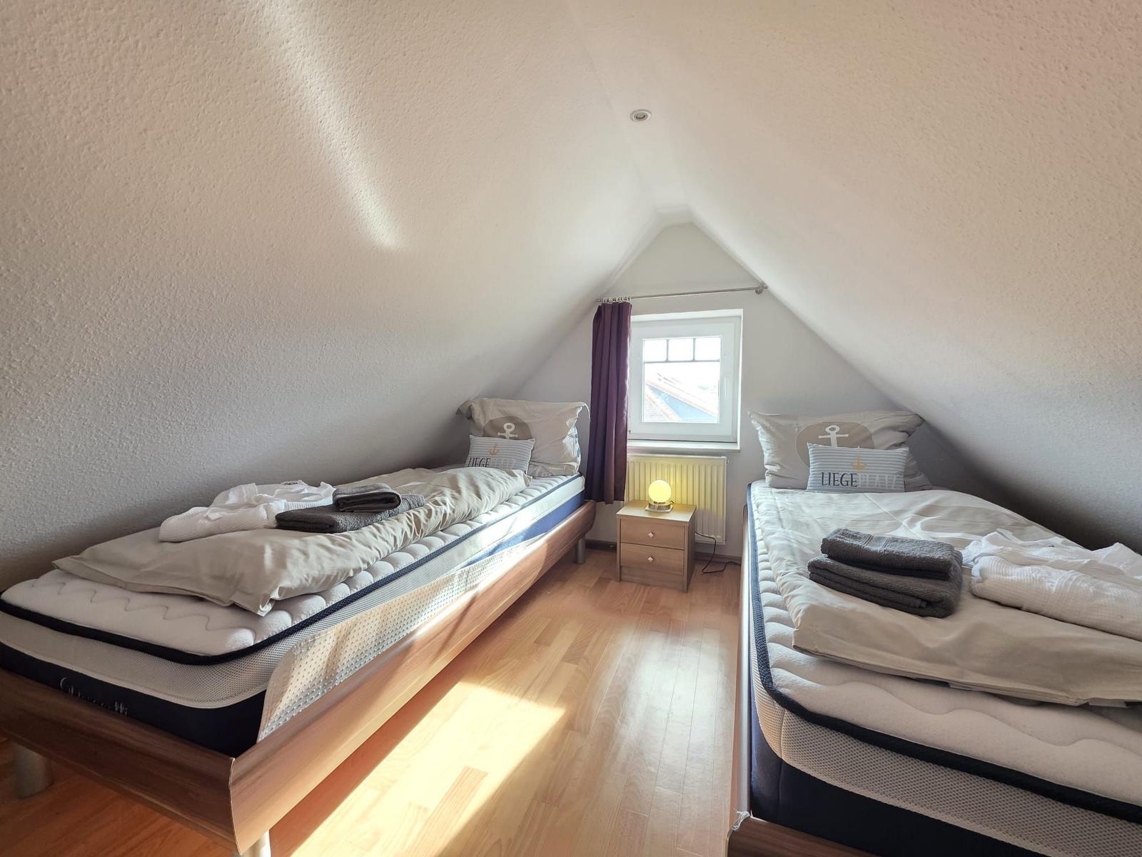 Two beds in an attic room with window and nightstand.