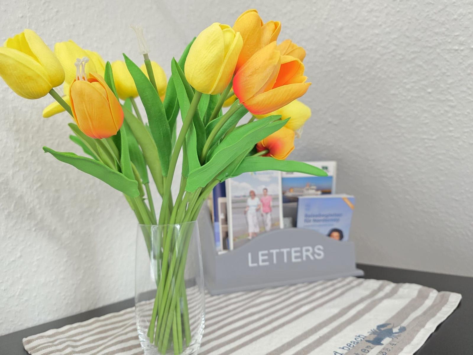 Tulips in vase on table with letter holder and tablecloth.