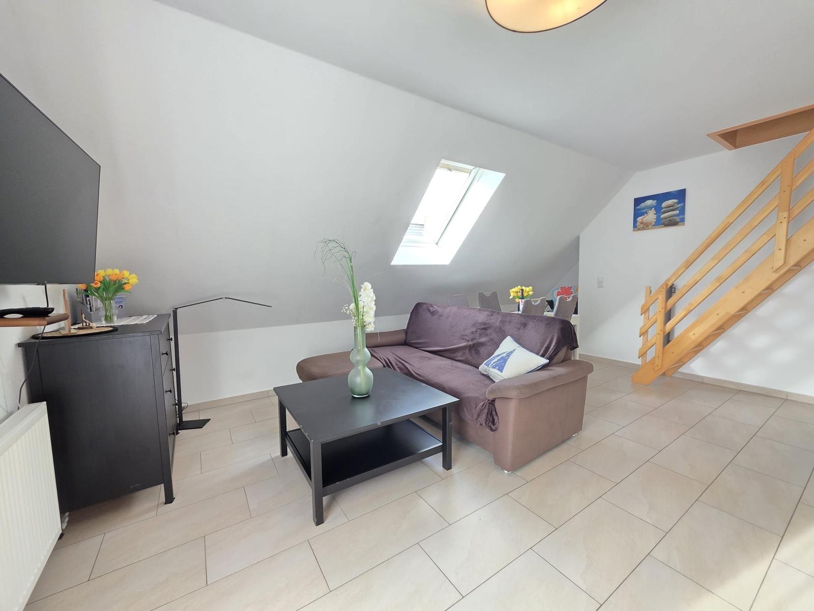 Living room with sofa, coffee table, and TV. Visible wooden staircase and skylight.