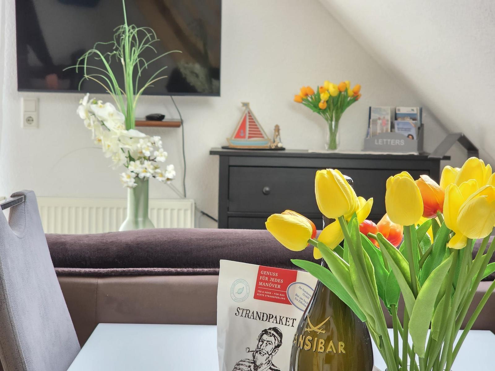 Living room with TV, flowers, and a table with tulips.