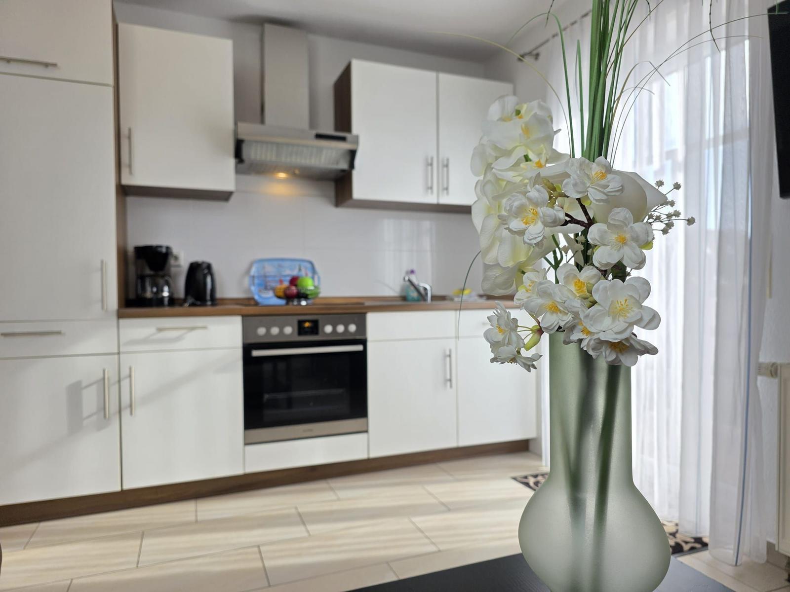 Kitchen with white cabinets, stove, and window with white curtains.