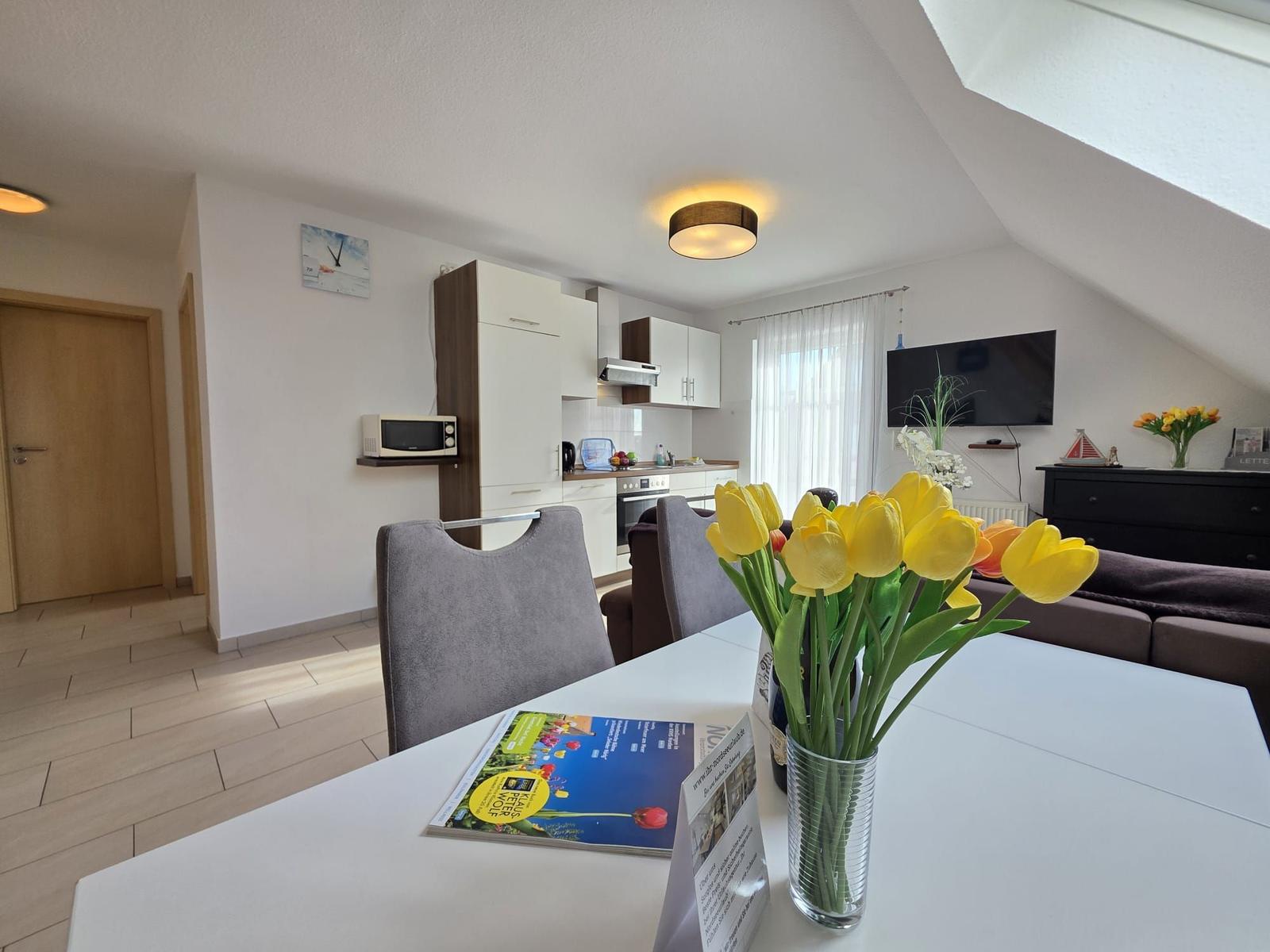 Living kitchen with dining table, TV, and cabinets under sloped ceiling