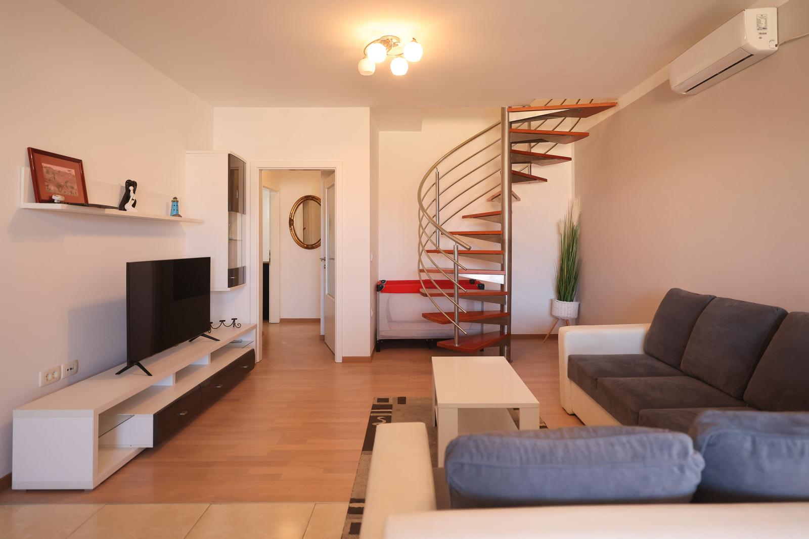 Wohnzimmer mit Sofa, Fernseher und Wendeltreppe.