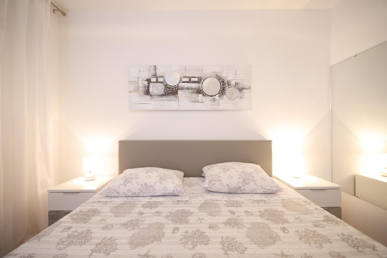 Schlafzimmer mit Bett, Nachttischen und Wandbild.