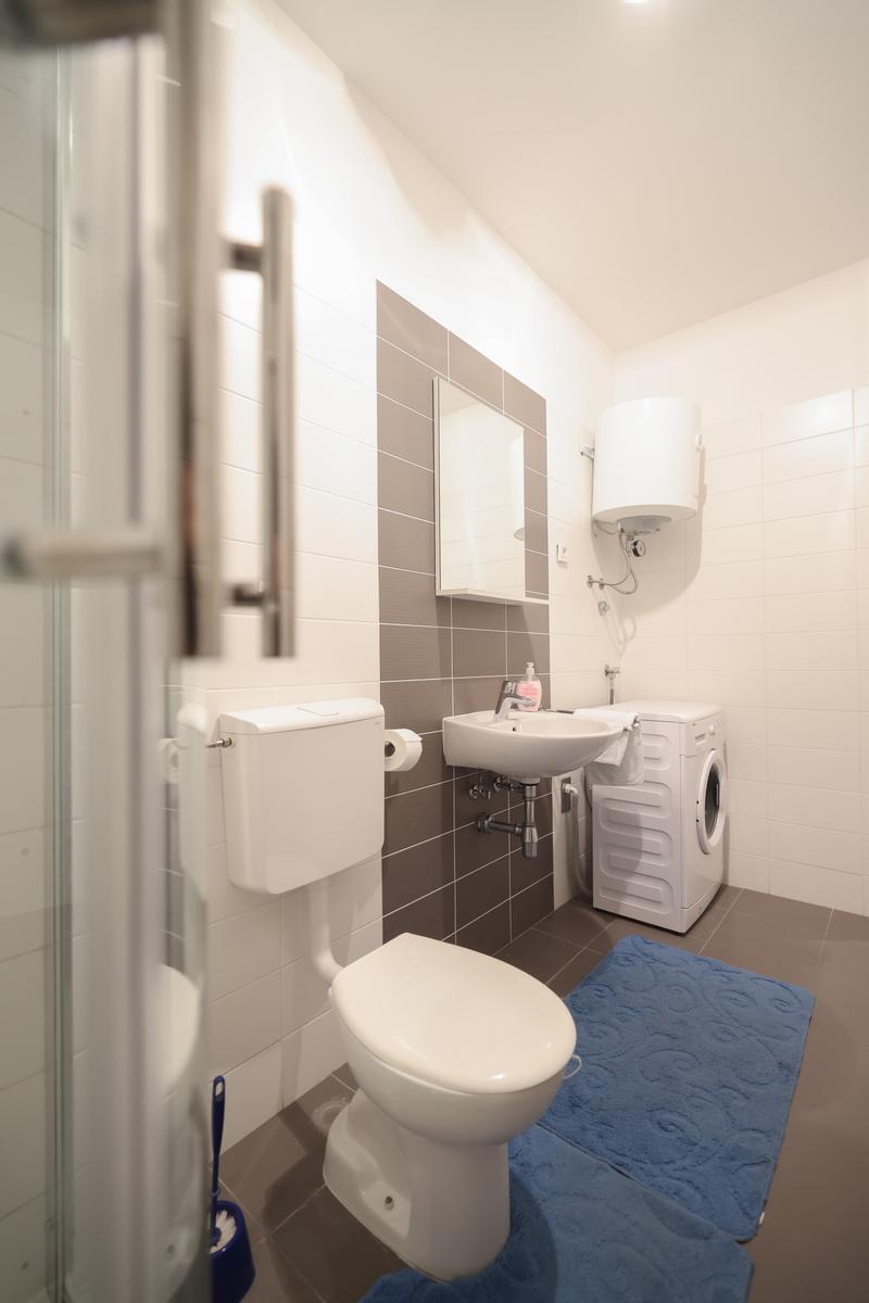 Badezimmer mit Toilette, Waschbecken, Spiegel und Waschmaschine.