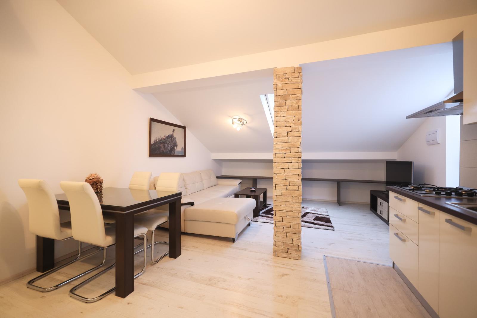 Wohn- und Essbereich mit Sofa, Tisch und Küchenzeile. Steinpfeiler trennt die Räume.