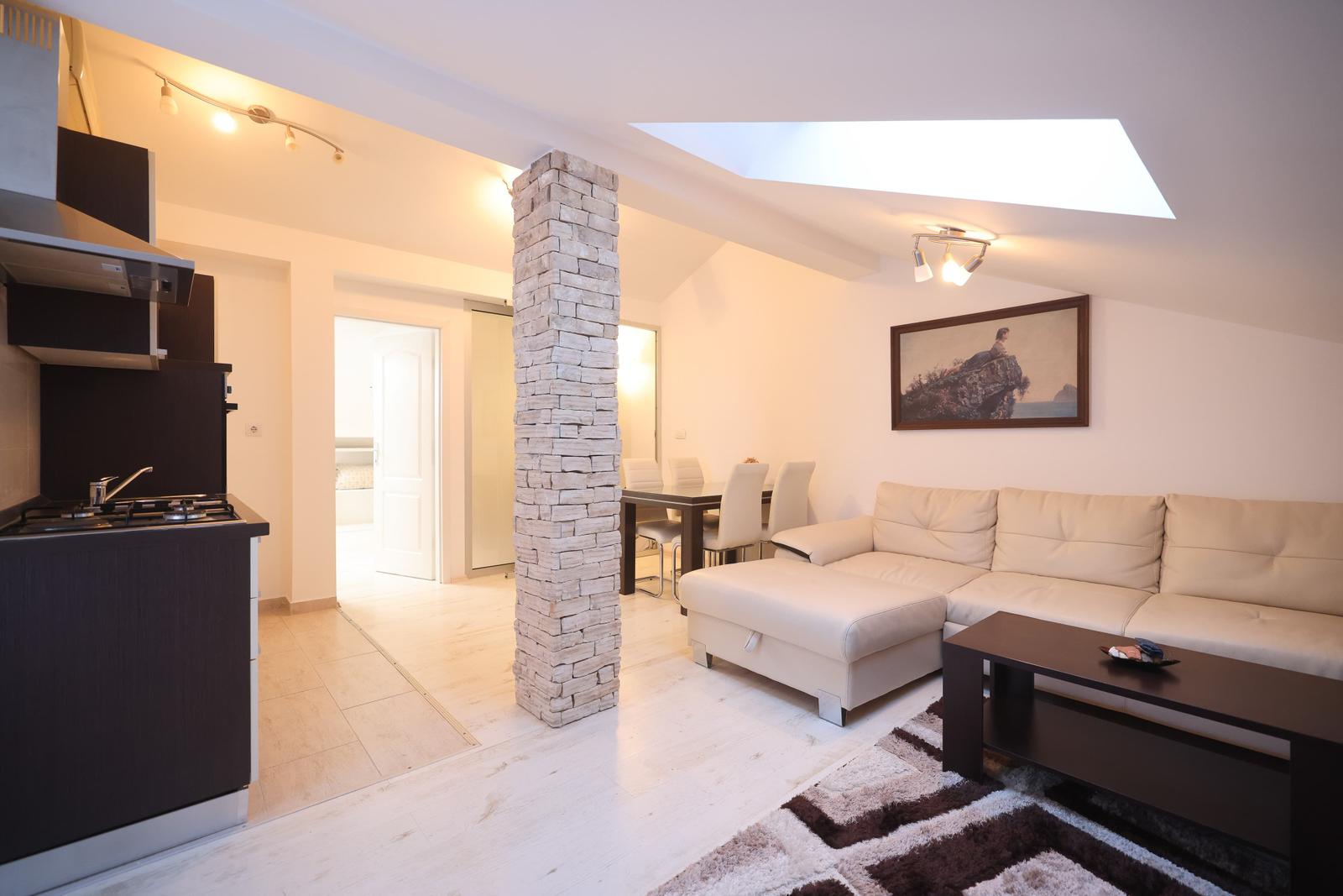 Wohnbereich mit Sofa, Esstisch und Küchenzeile. Steinpfeiler und Dachfenster.