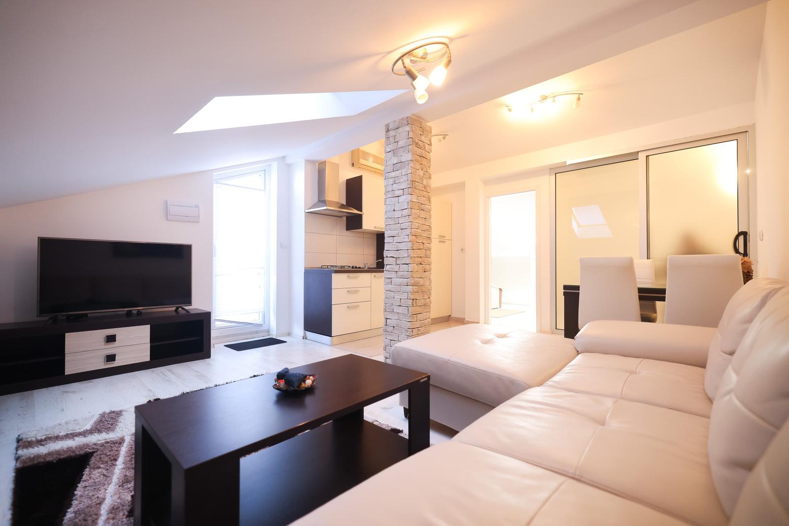 Wohnzimmer mit Sofa, Couchtisch und TV. Küche und Schlafzimmer sind sichtbar.