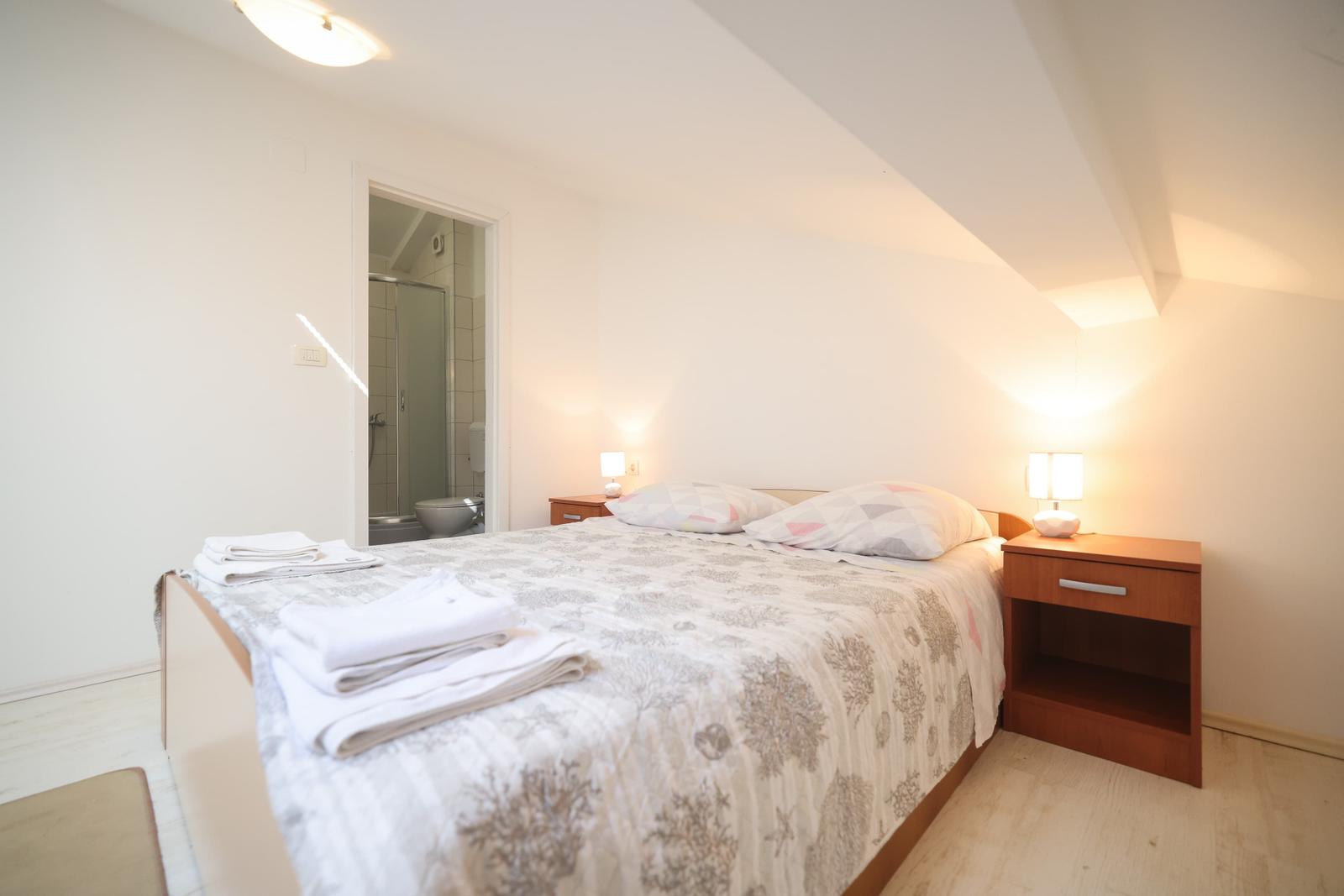 Schlafzimmer mit Bett, Nachttischen und Bad im Hintergrund.