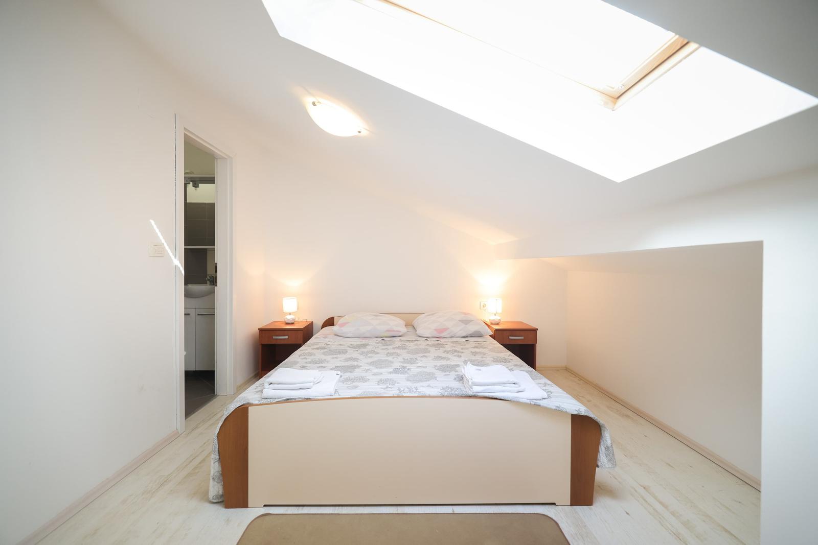 Schlafzimmer mit Dachschrägen, Dachfenster, Bett und Nachttischen.