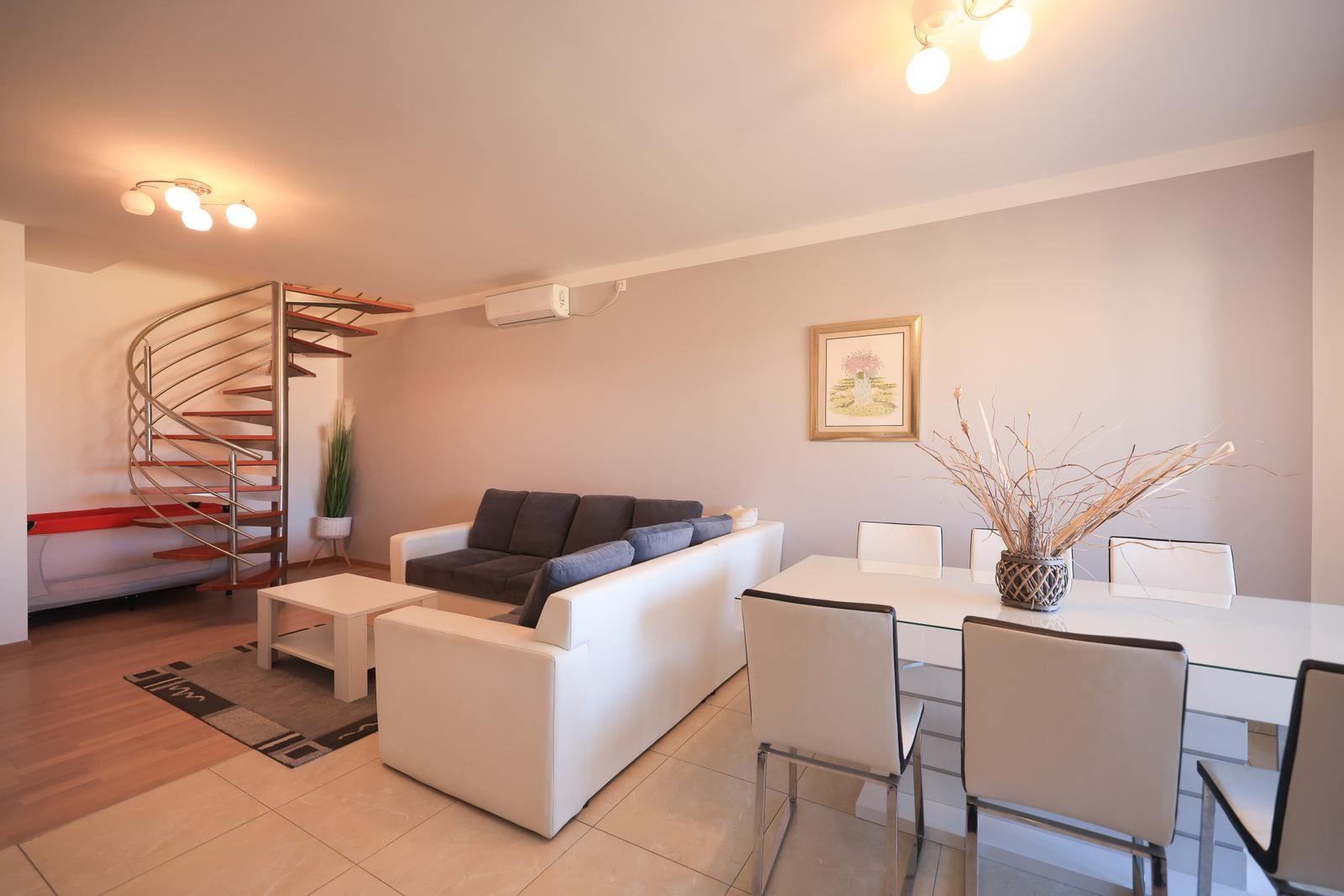 Wohn- und Essbereich mit Sofa, Tisch und spiralförmiger Treppe.