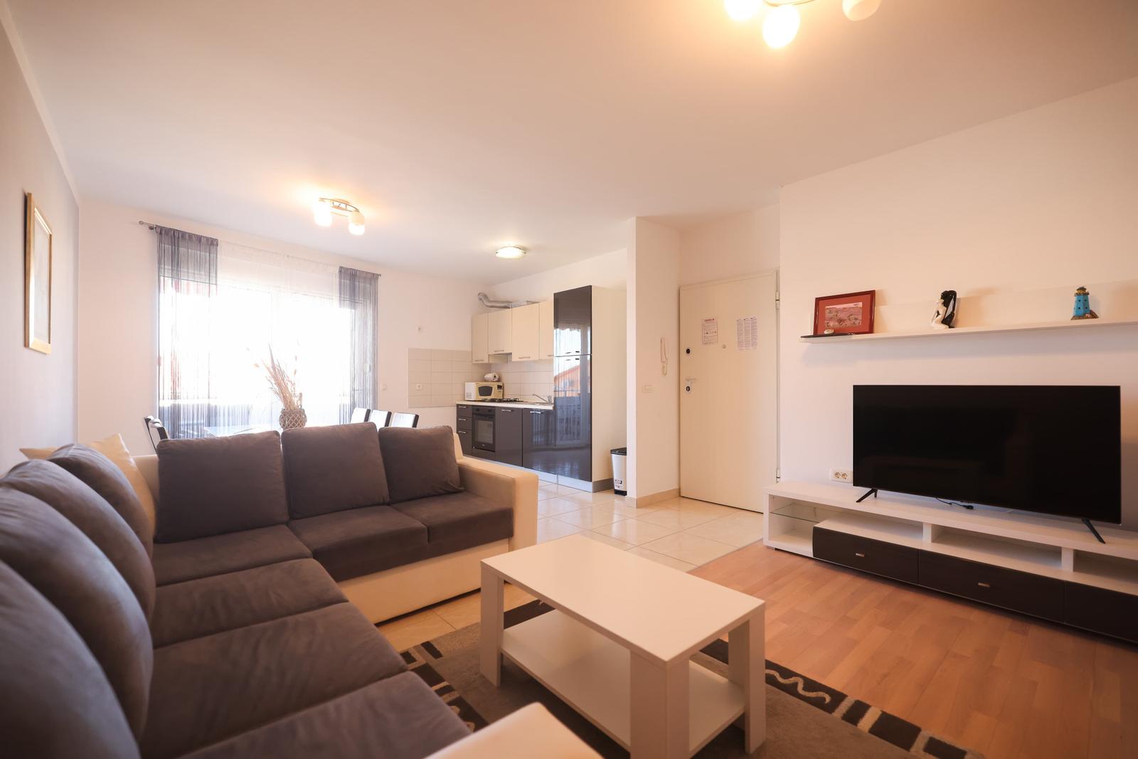 Wohnzimmer mit Sofa, Fernseher und Küche im Hintergrund.