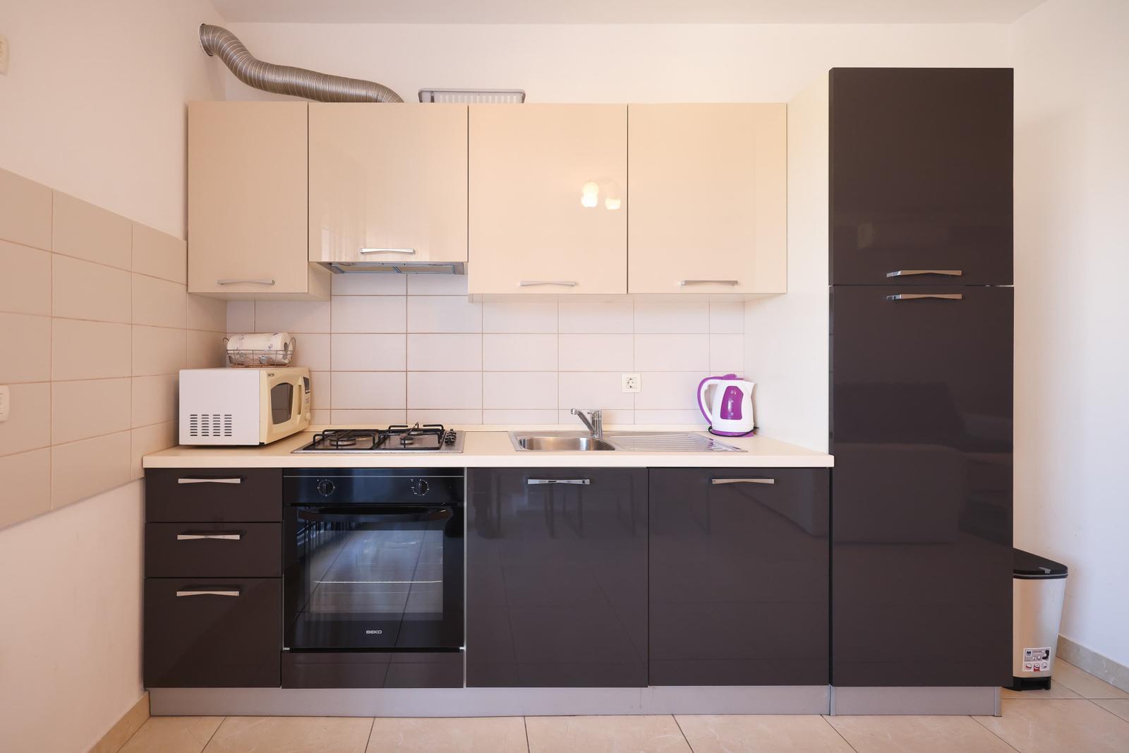 Küche mit dunklen Schränken, Herd, Spüle und Kühlschrank.