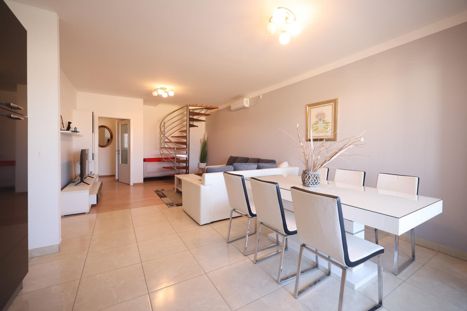 Wohn- und Essbereich mit Esstisch, Sofa und Wendeltreppe.