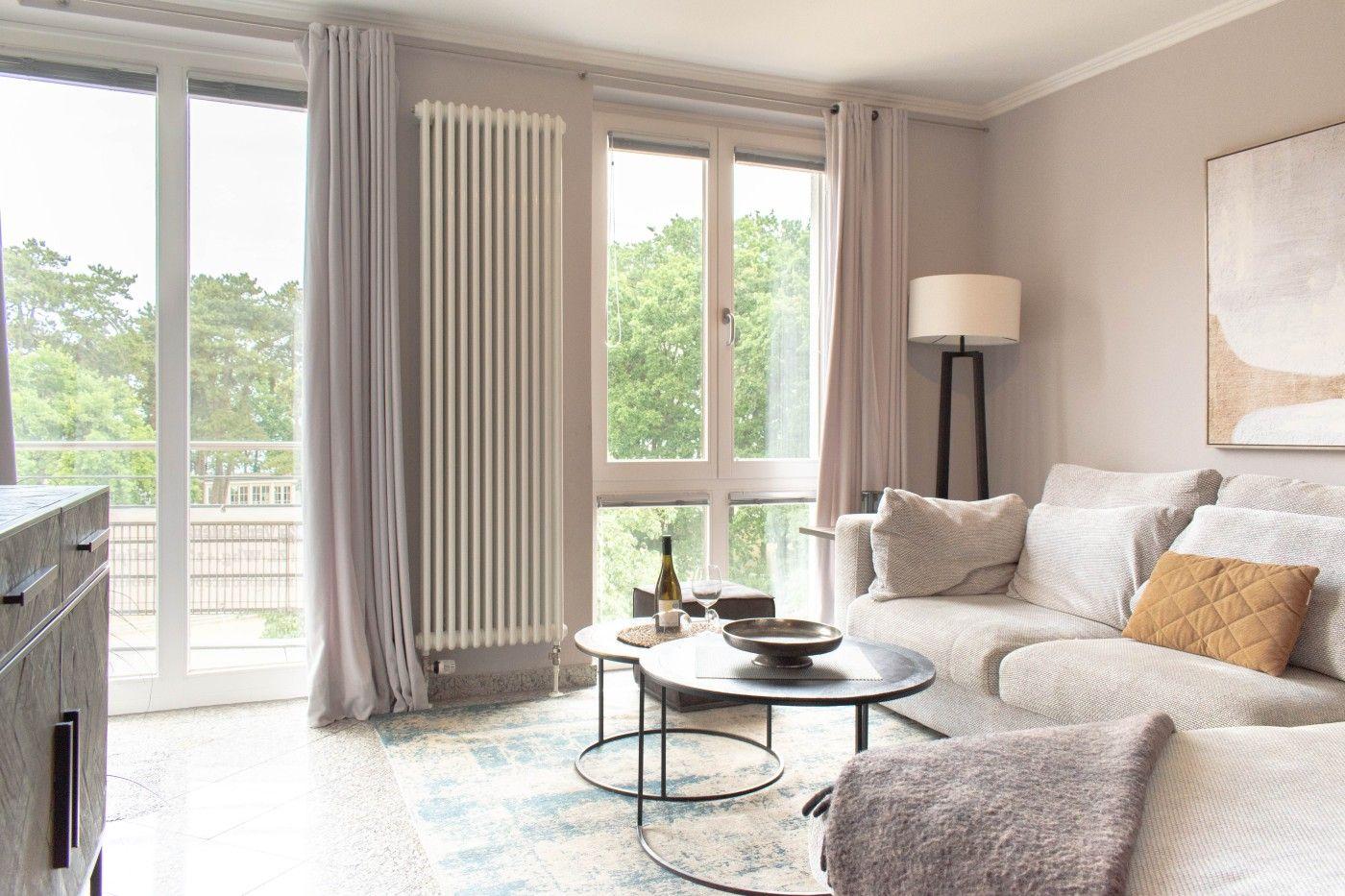 Wohnzimmer mit Sofa, Couchtisch und Blick auf Balkon mit Bäumen.