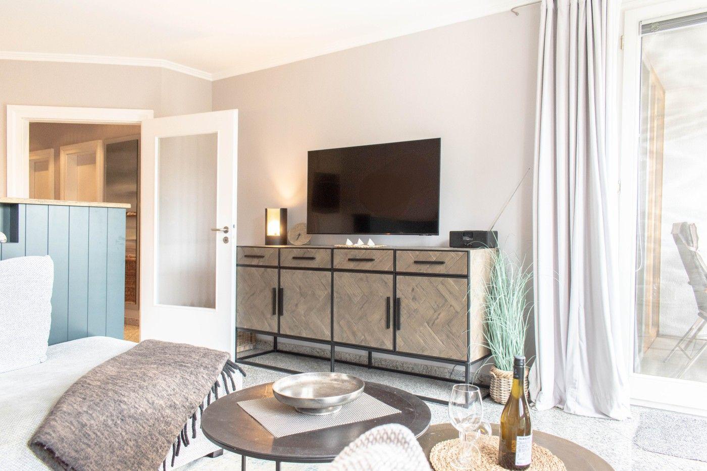 Wohnzimmer mit TV, Couch und Tisch. Durchgang zur Küche. Terrasse mit Blick.