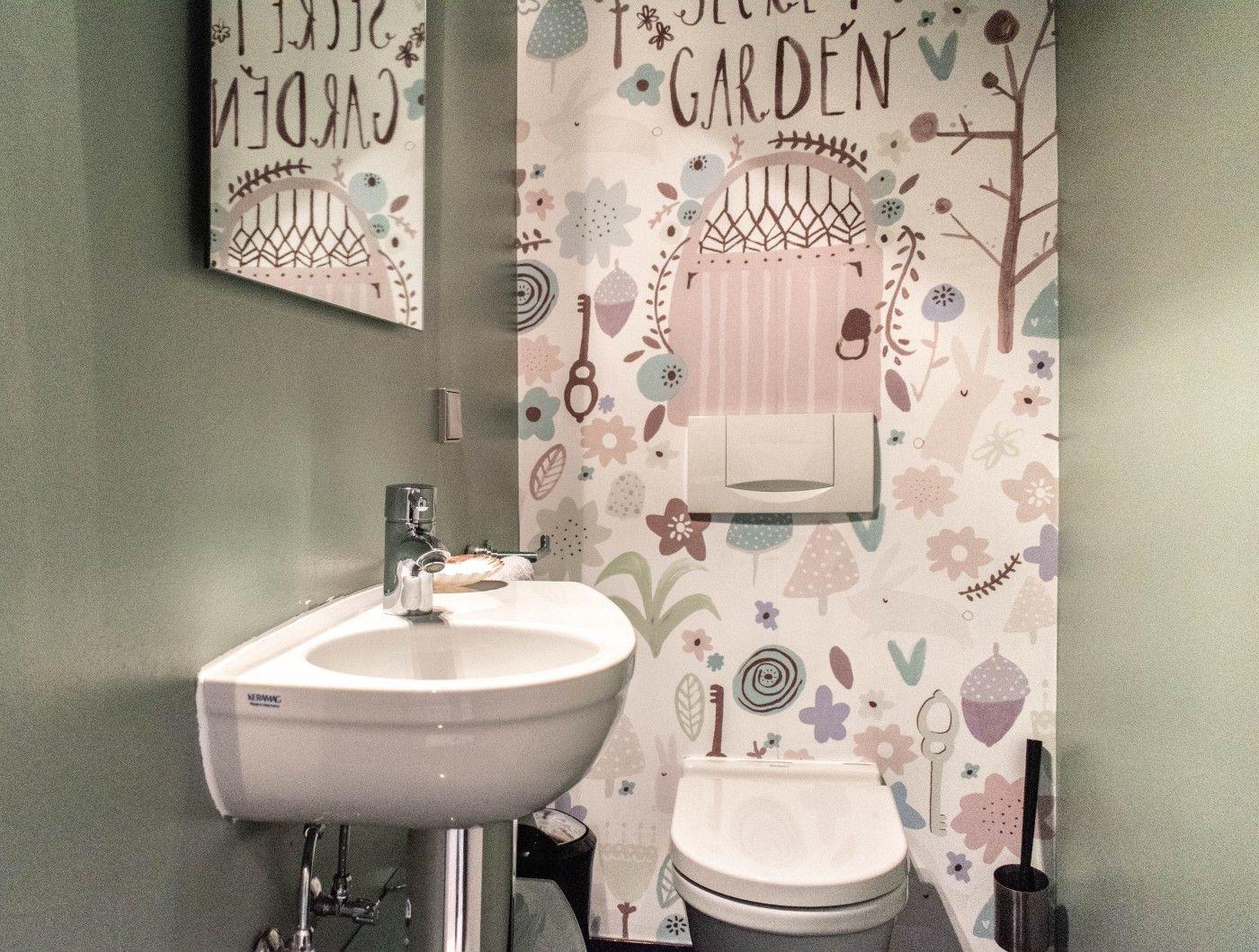 Badezimmer mit Waschbecken, Toilette und gemustertem Wandbehang.