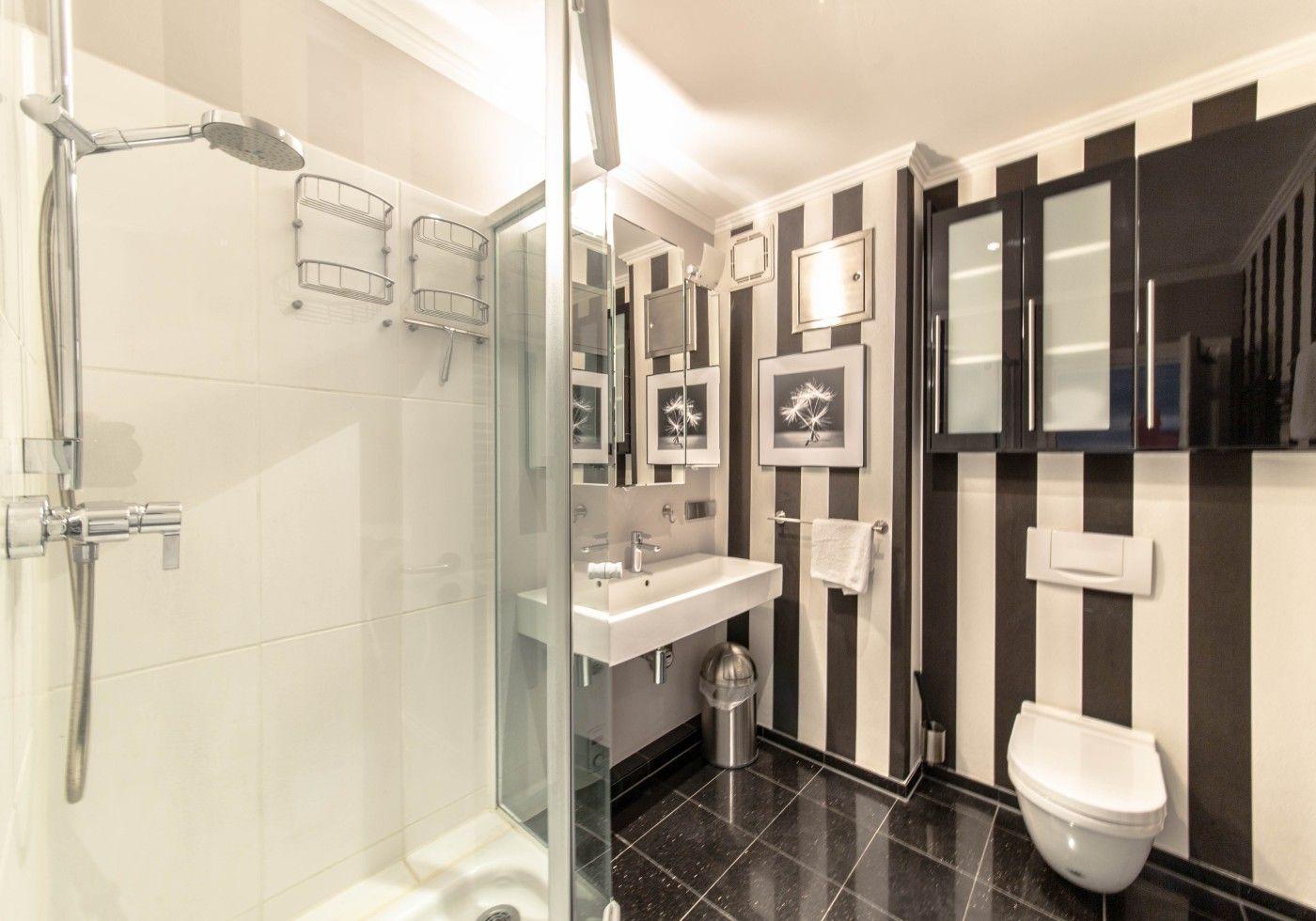 Badezimmer mit Dusche, Waschbecken und Toilette. Wand mit schwarz-weißen Streifen.