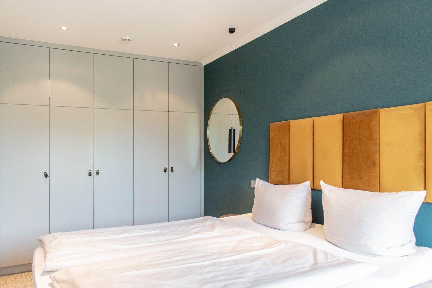 Schlafzimmer mit Bett, goldfarbenem Kopfteil und Kleiderschrank an der Wand.